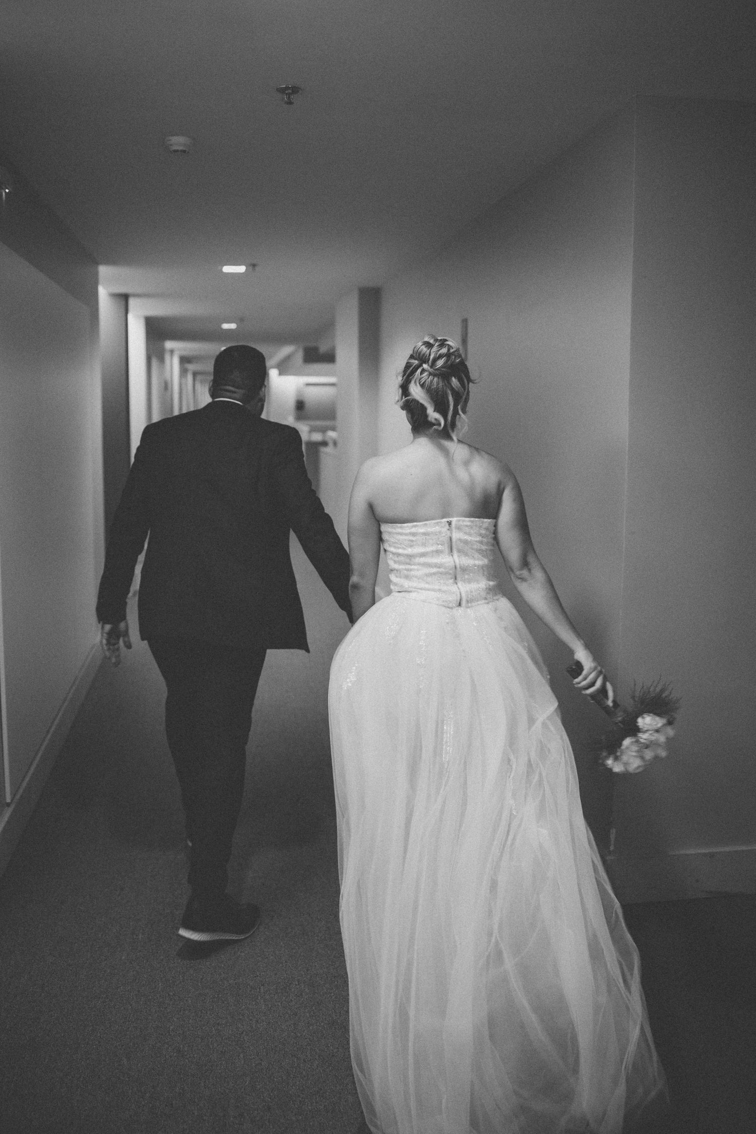 A black and white photo of a couple walking down a dimly lit hallway.