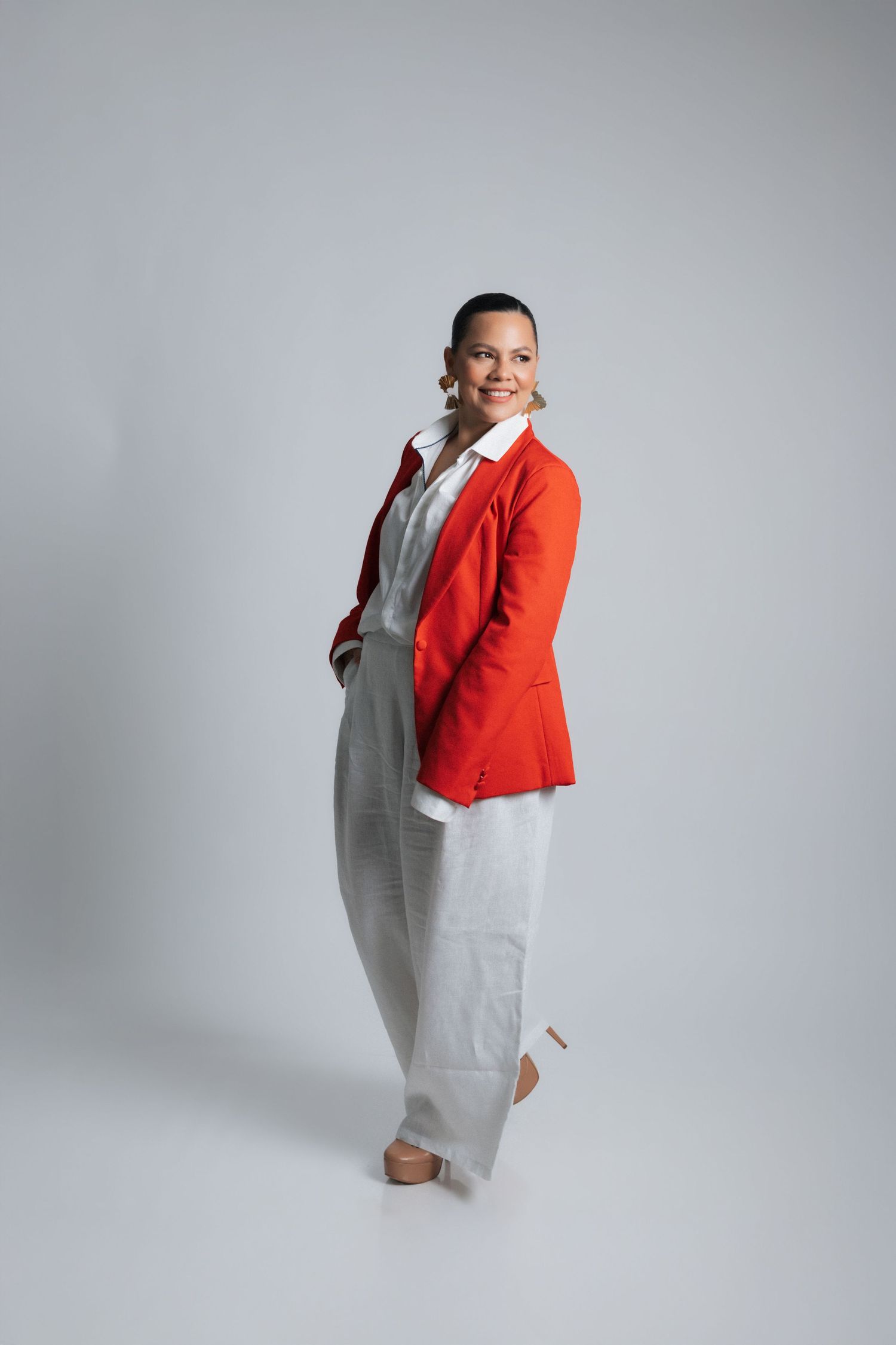 Full-length fashion portrait showing a red blazer paired with white pants and nude heels in a studio setting.