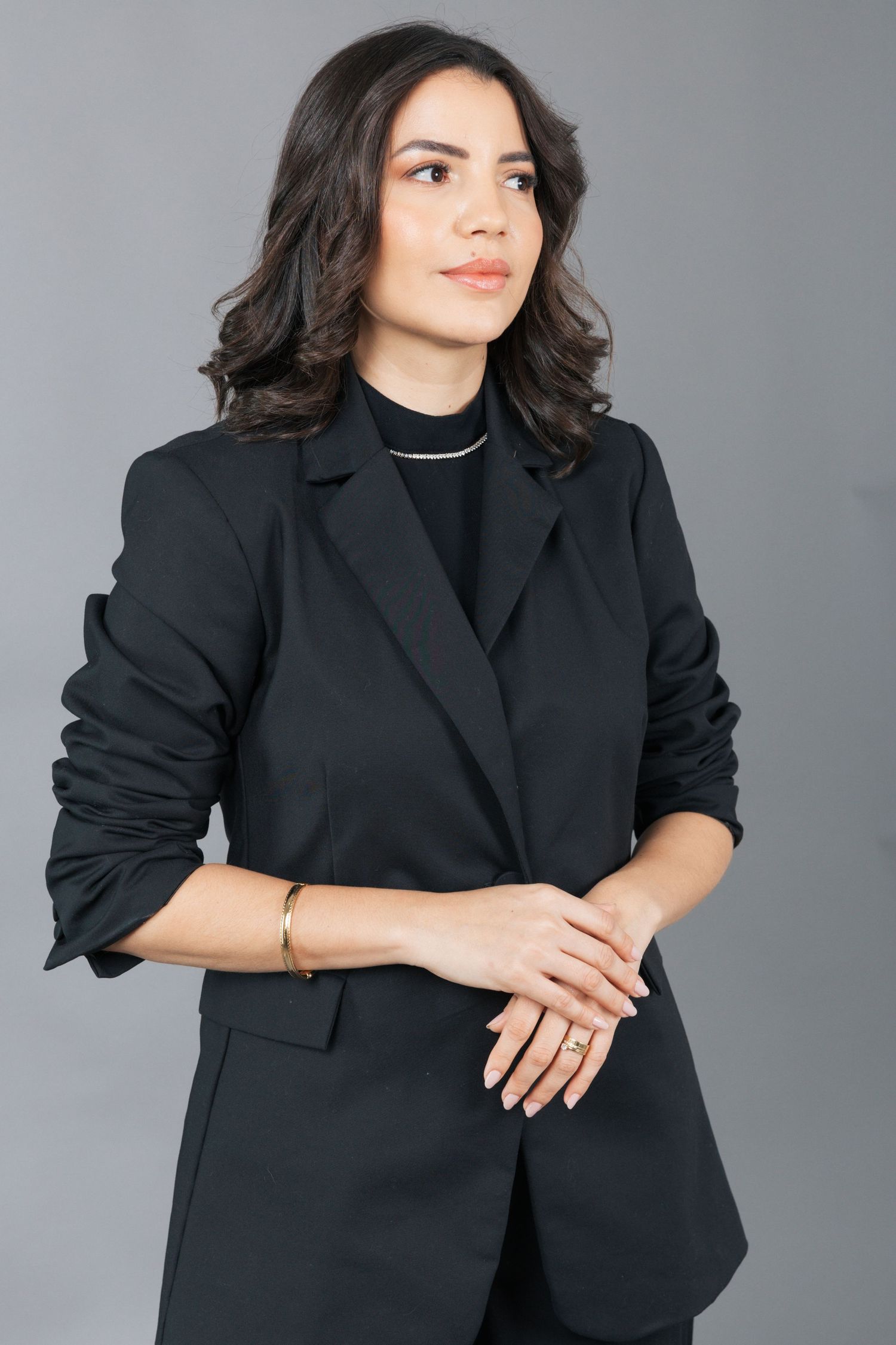 Elegant portrait in black blazer and turtleneck against gray studio background.