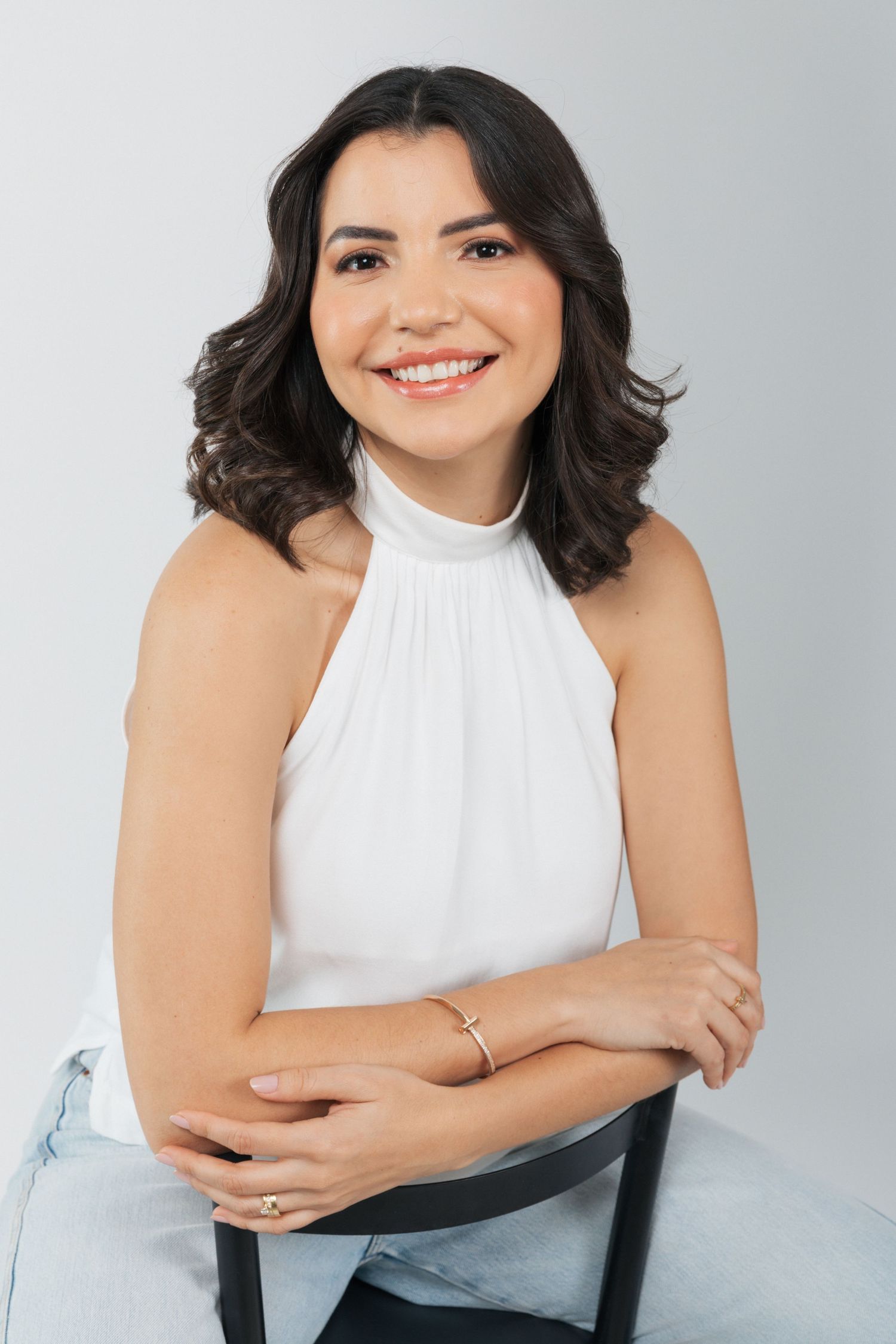 Professional portrait in white halter top showing warm smile against light background.