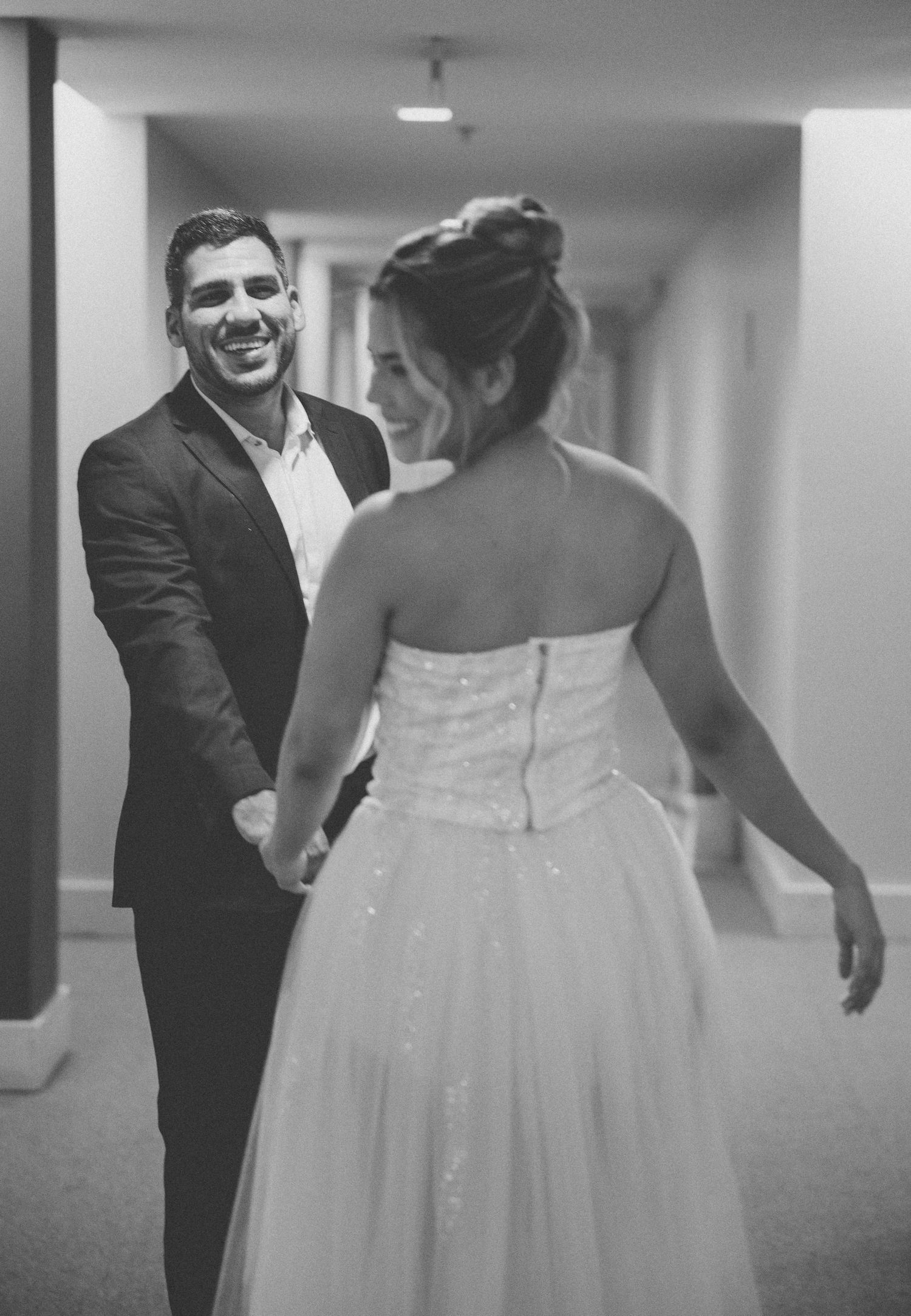 Black and white photograph showing a first look between a groom in a dark suit and bride in a strapless white wedding gown.