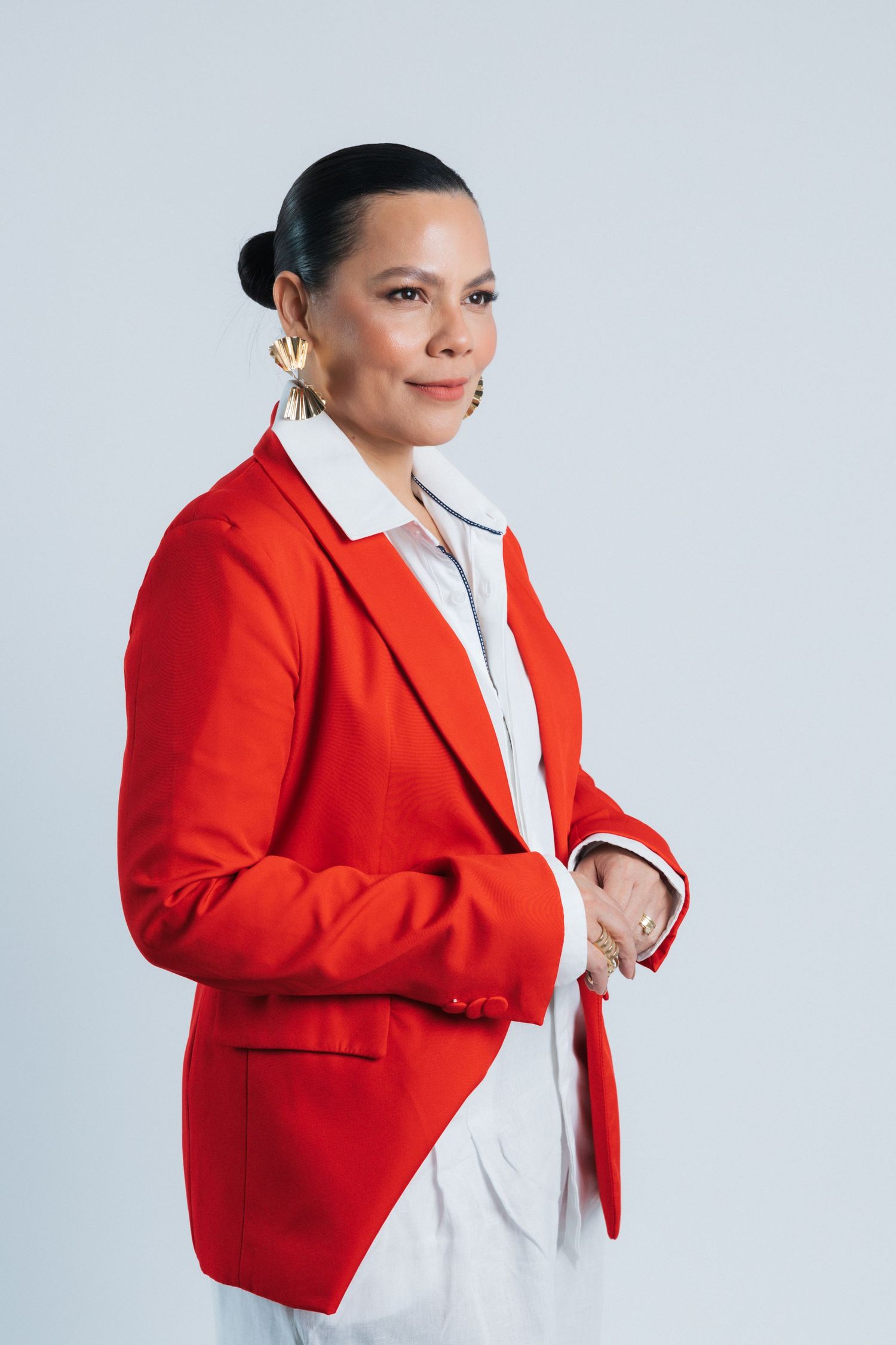Elegant studio shot of model in bright red blazer and white outfit against light background.