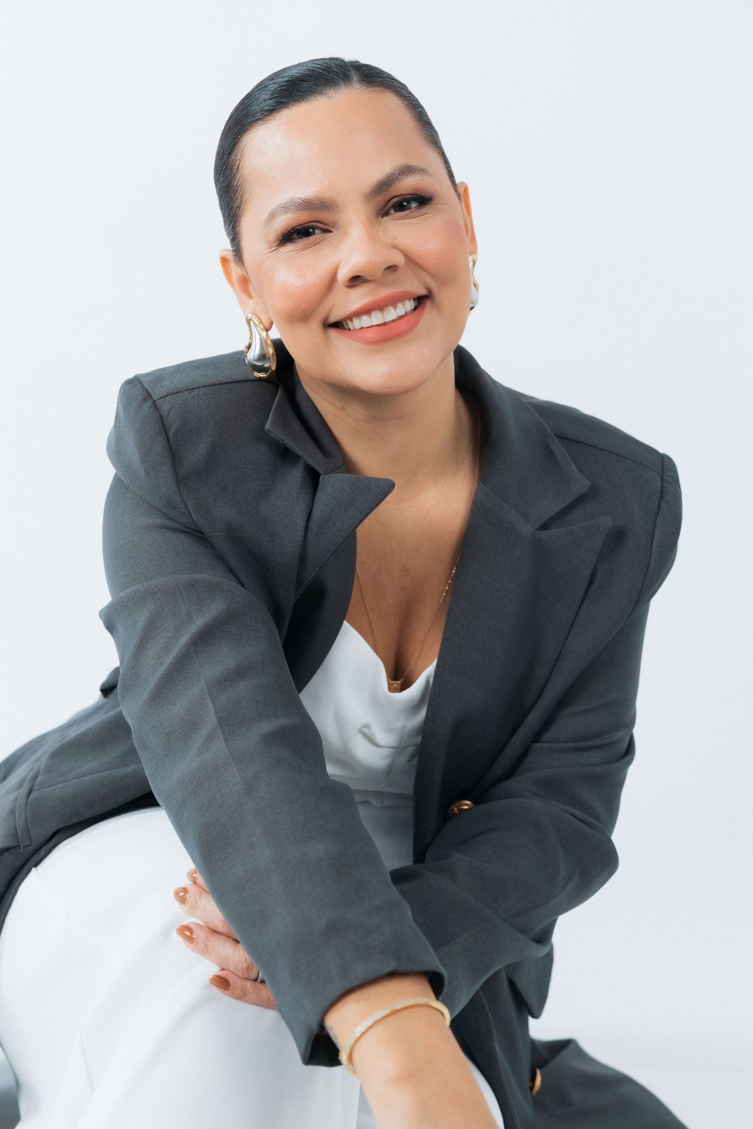 Professional portrait of someone in a dark blazer and white top smiling against a light background.