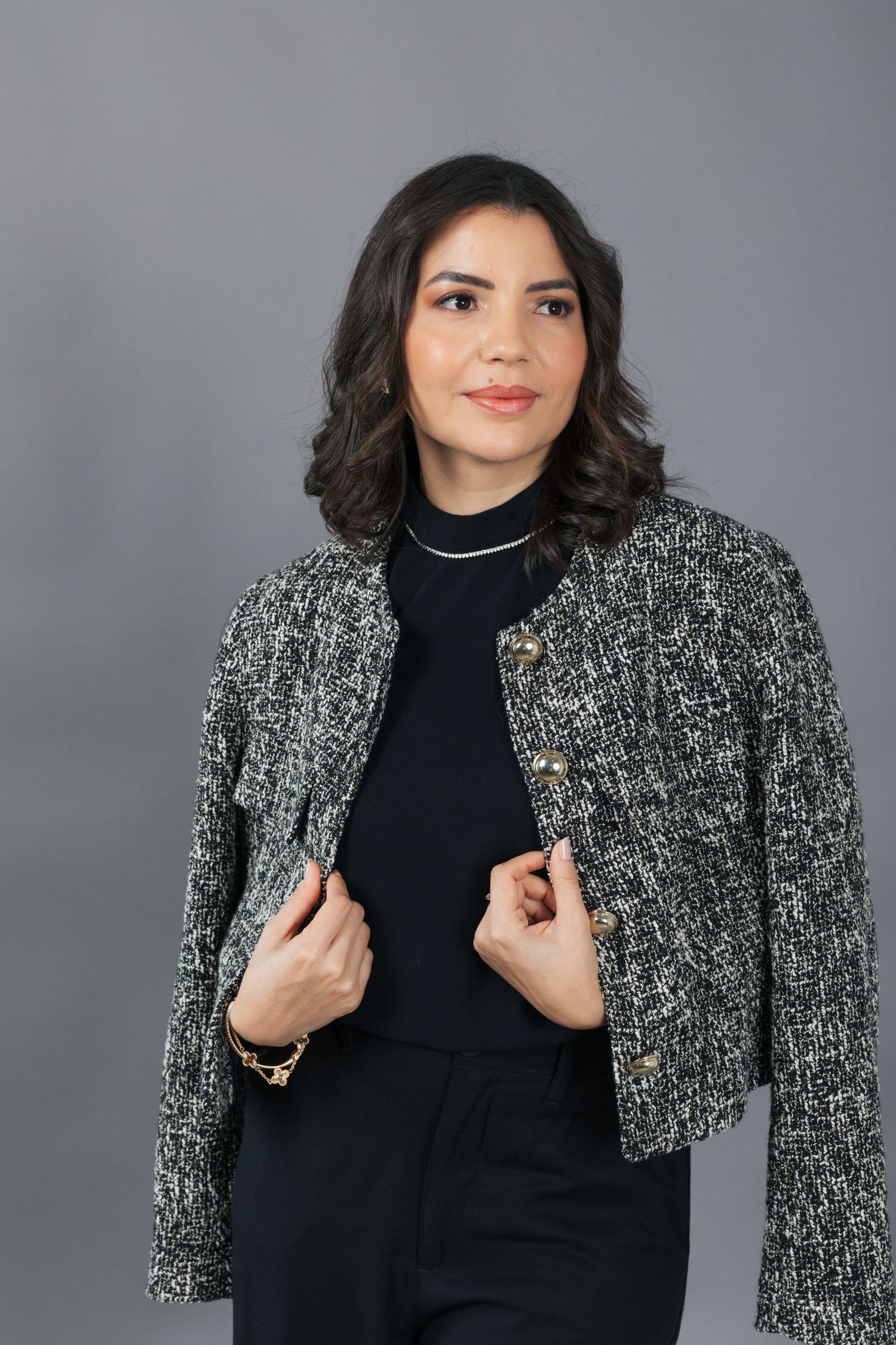 Stylish woman posing in a black turtleneck and textured gray jacket against a neutral background.