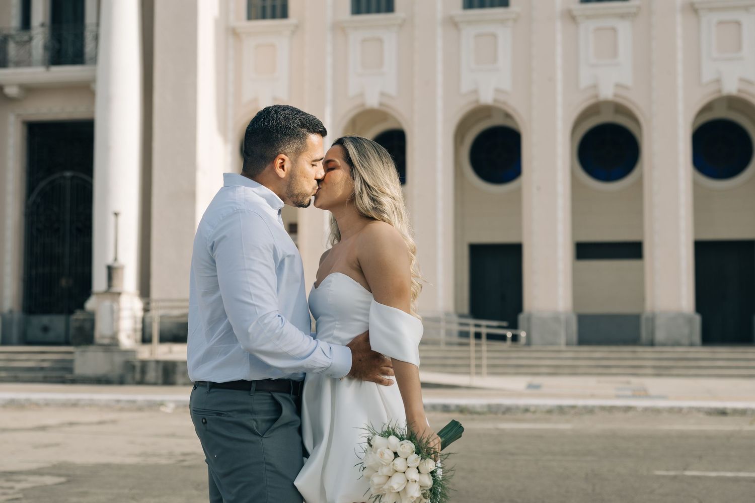 Couple shares an intimate moment outside a historic building with white columns and circular windows.