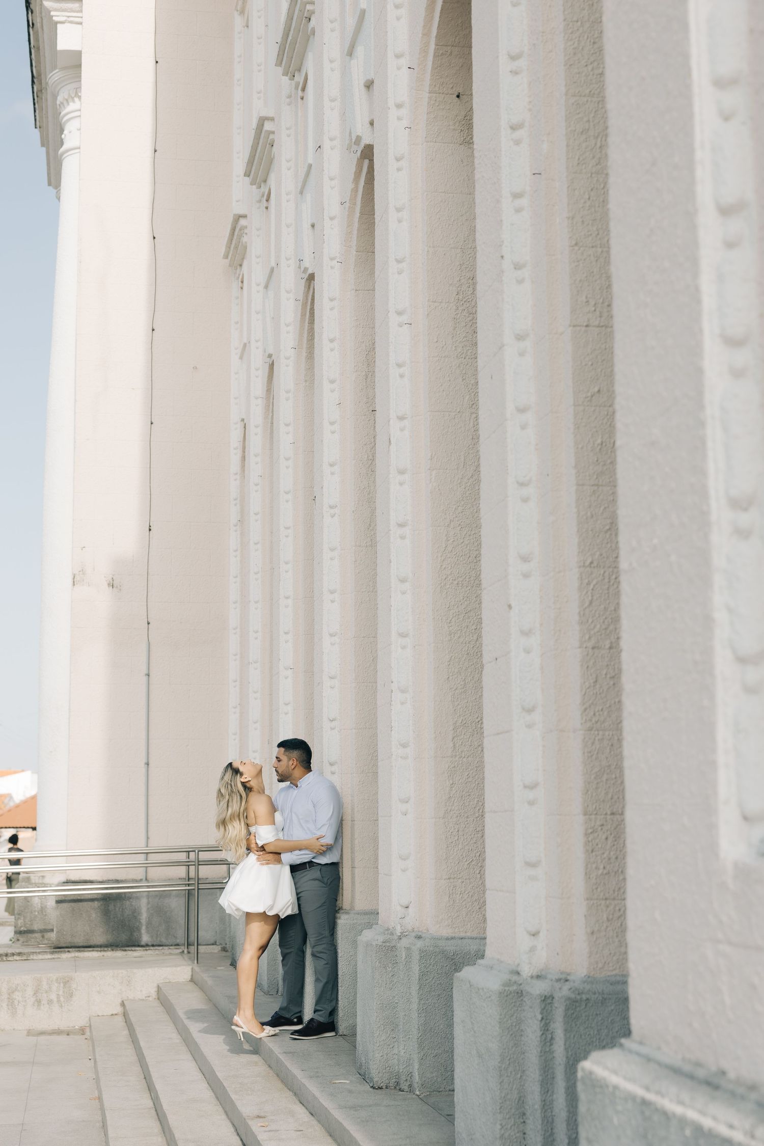 A couple shares a romantic moment between tall white columns of a classical building exterior.