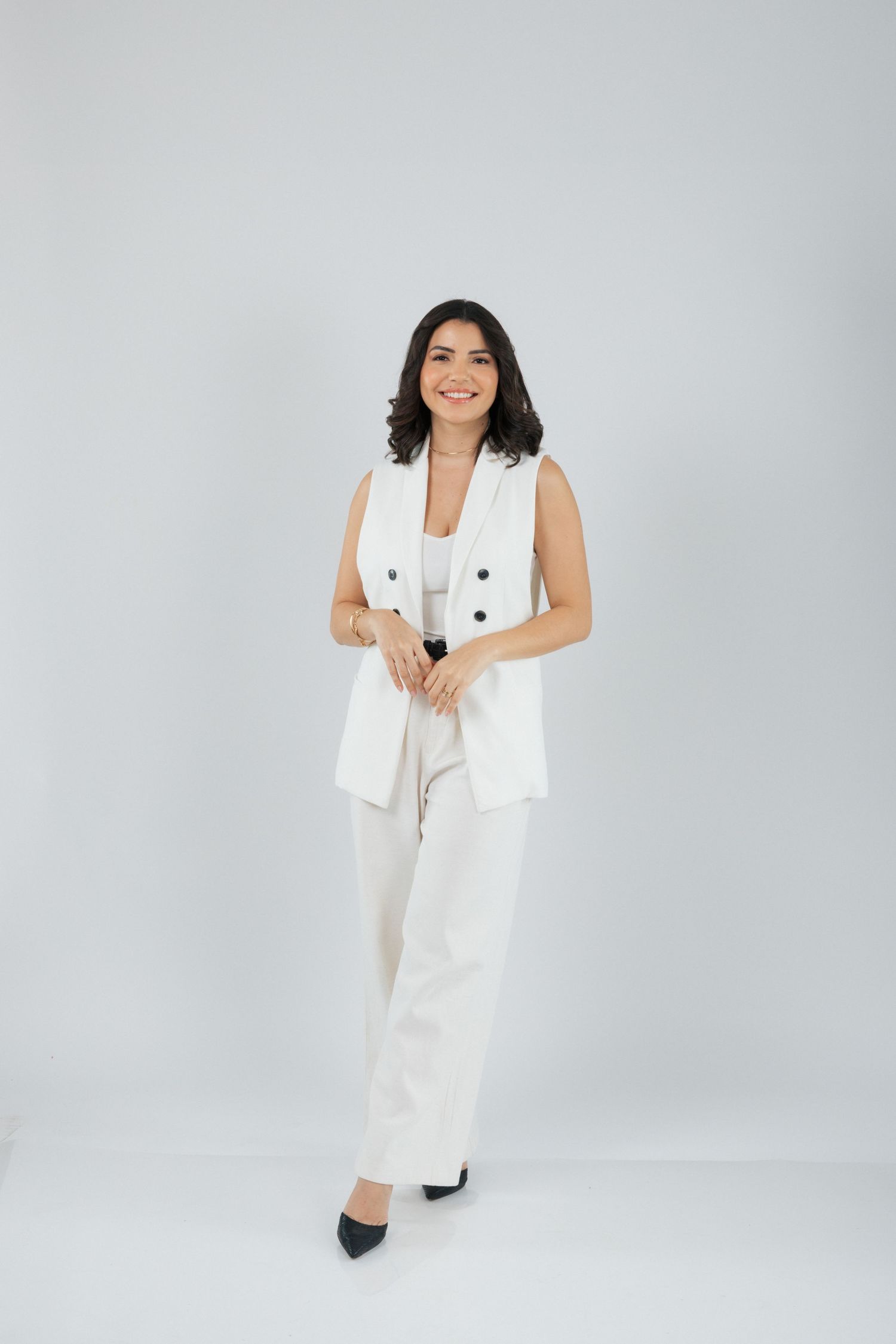 Full body portrait in crisp white business outfit with vest and trousers against light backdrop.