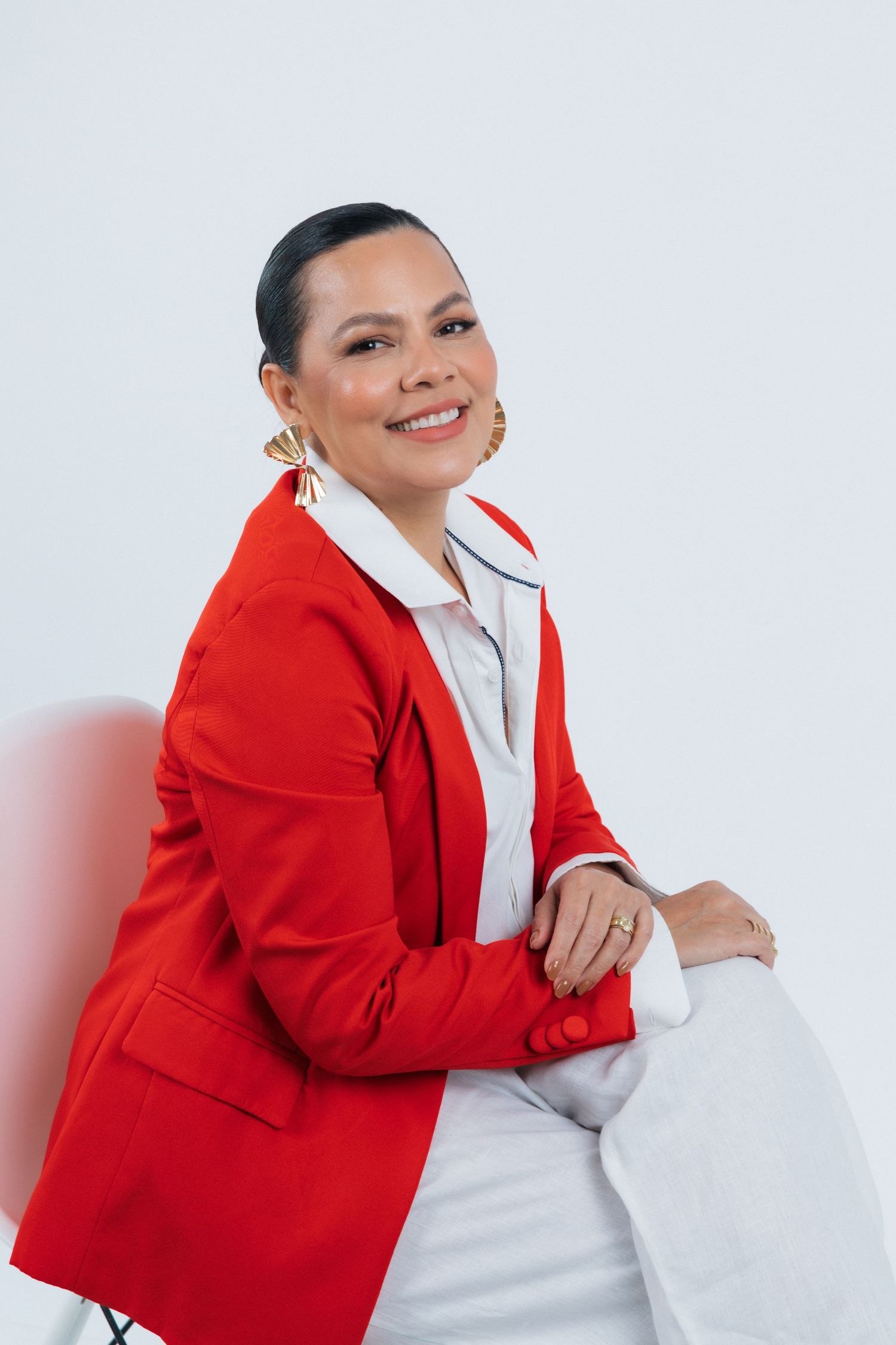 Professional portrait of a smiling woman wearing a vibrant red blazer and white blouse against a light background.
