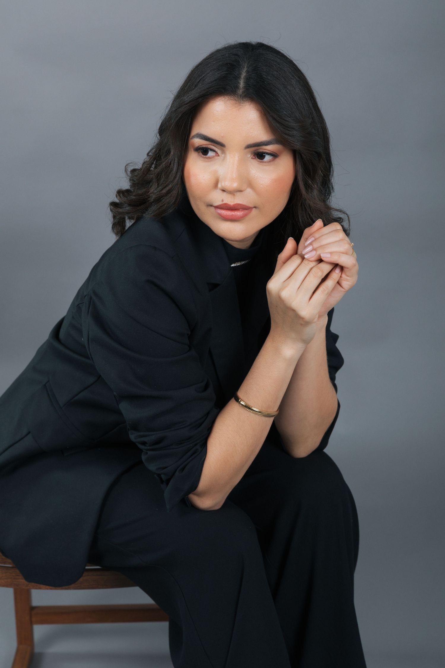 Elegant portrait of a woman in black attire seated thoughtfully with clasped hands.