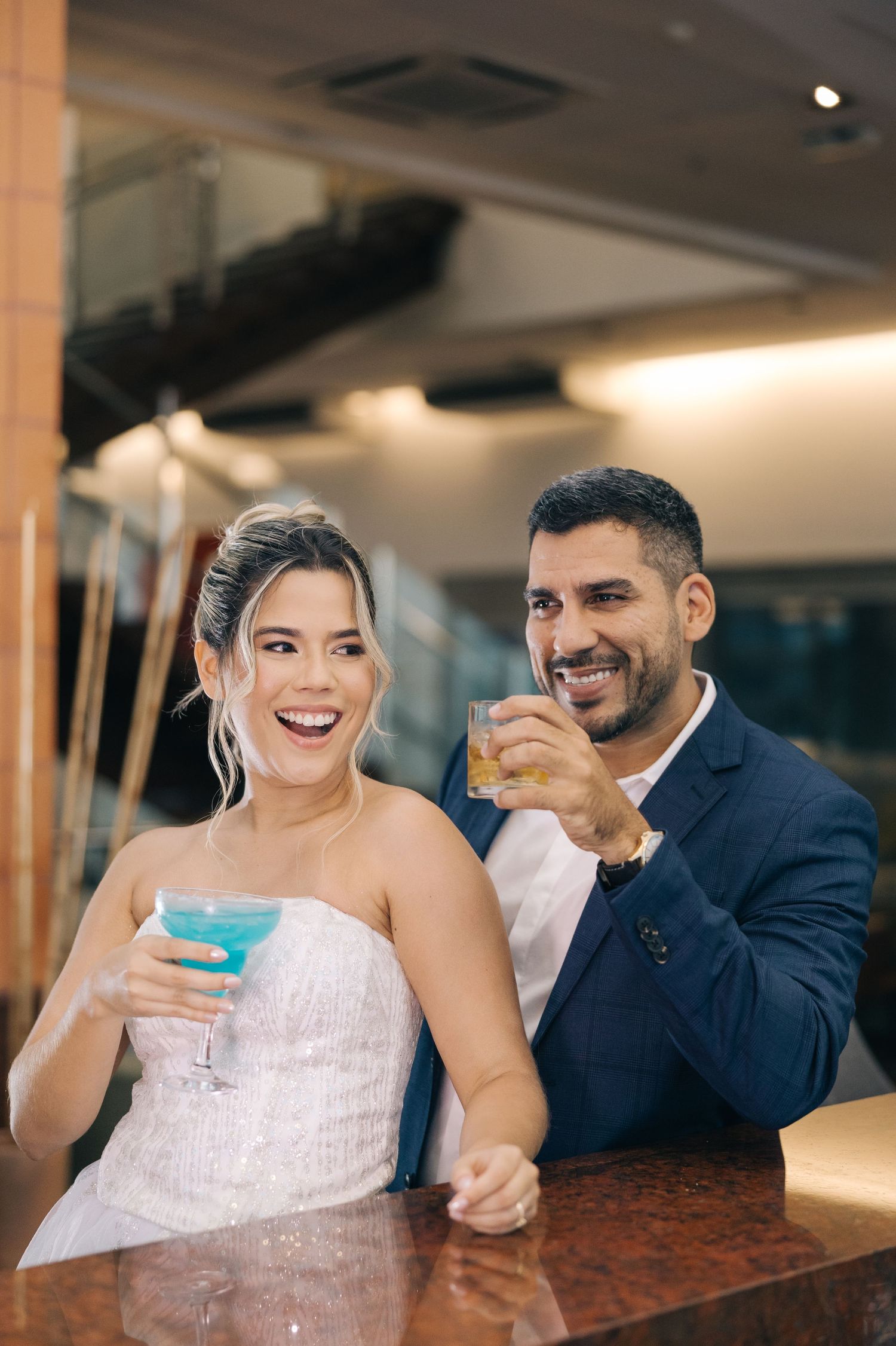 A couple shares cocktails and laughs at an elegant bar with wooden details.