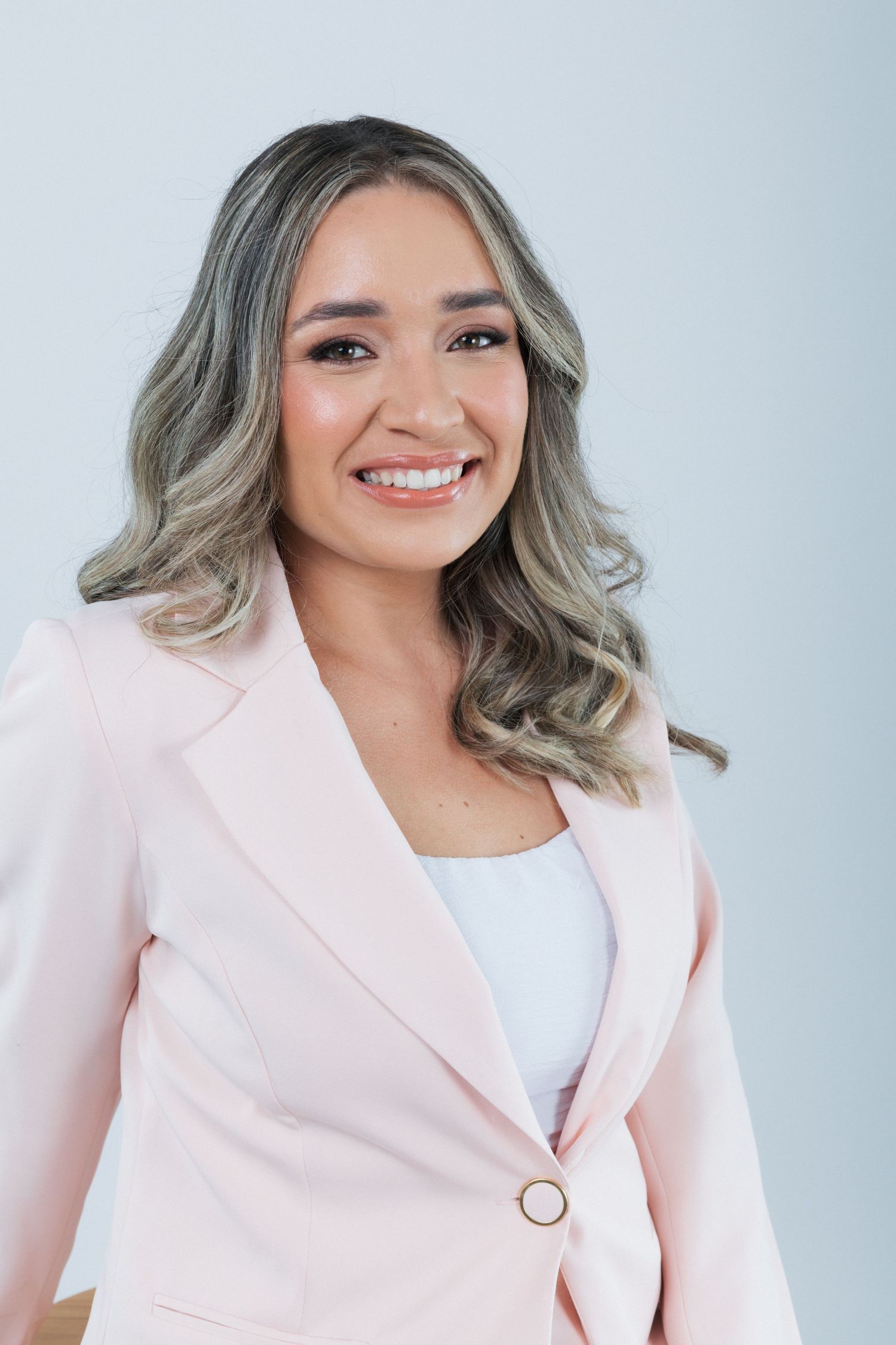 Professional business portrait of a person wearing a light pink blazer and white top with wavy silver-toned hair.