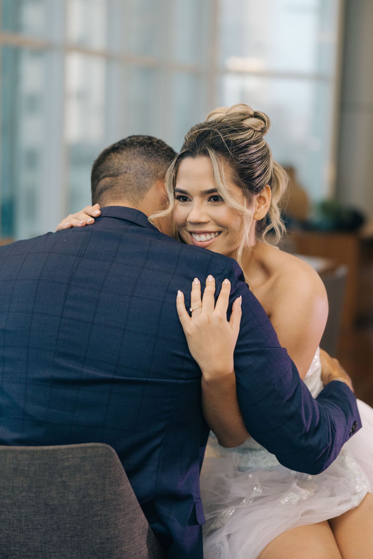 Tender embrace during an indoor celebration with soft window lighting.