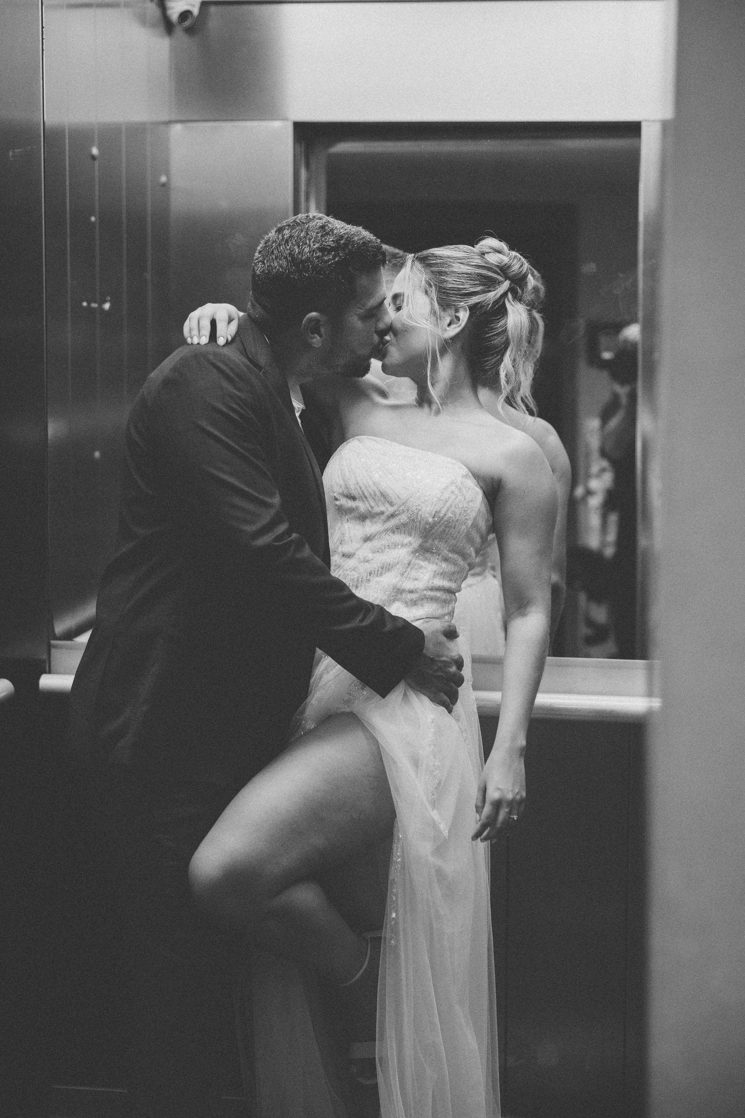 A romantic black and white portrait of newlyweds sharing an intimate moment in an elevator.