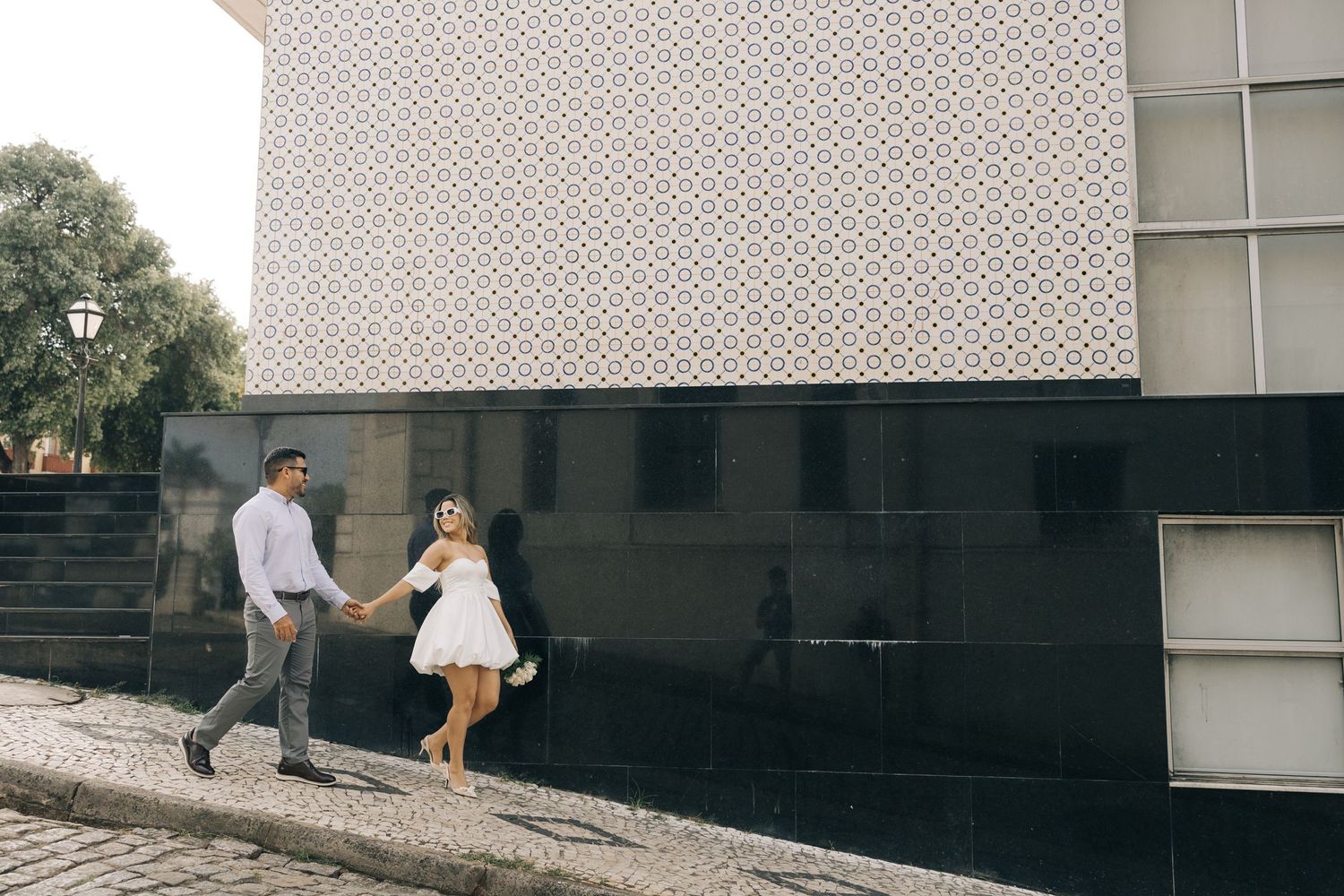 A couple strolls along a modern building exterior with textured walls.