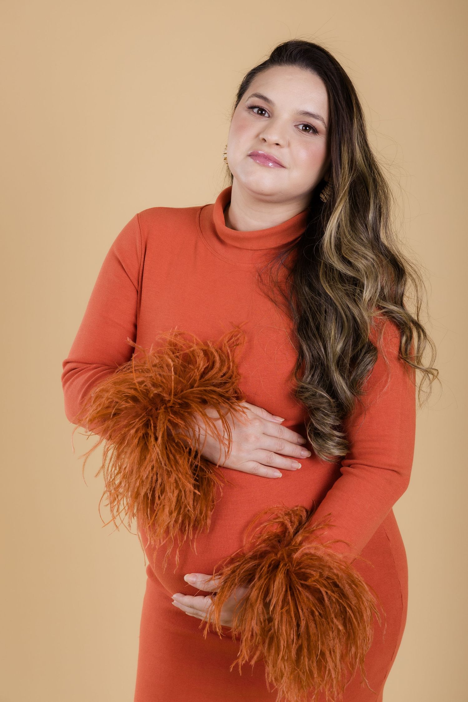 Woman in orange turtleneck dress with fluffy rust-colored fur cuffs poses against beige background.