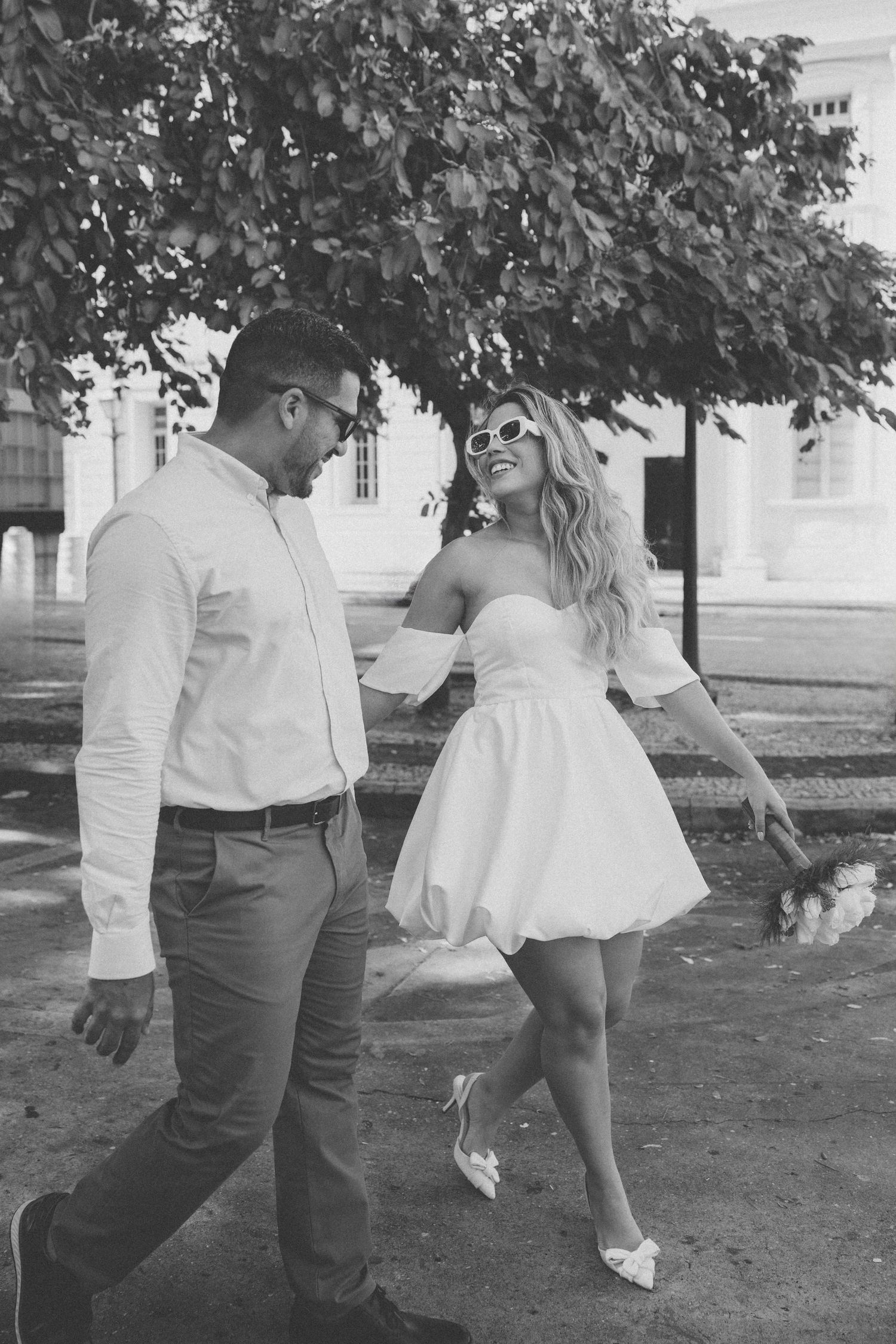 A playful dance moment captured in black and white near a leafy tree.