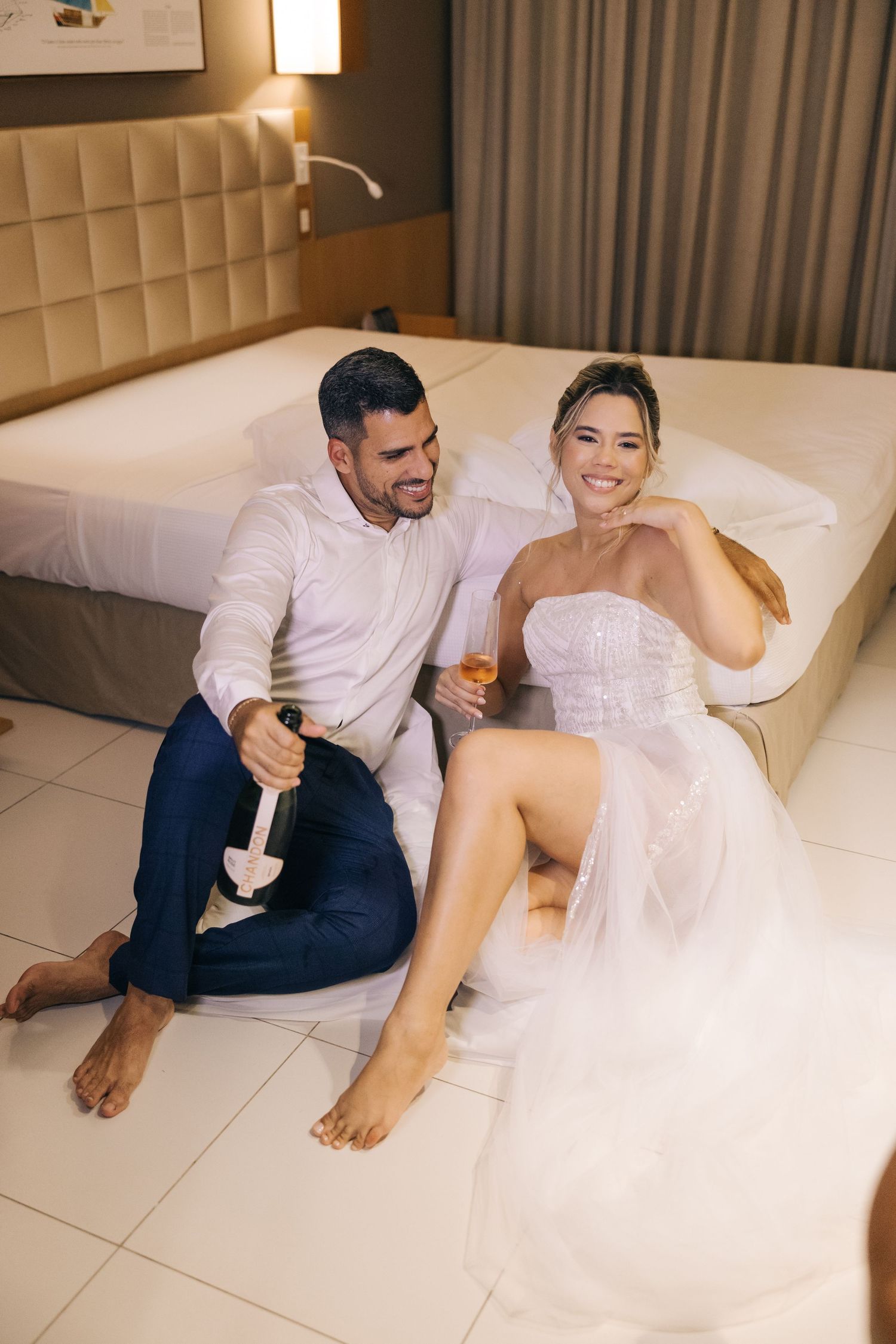 A couple enjoys champagne while relaxing on a plush hotel bed.