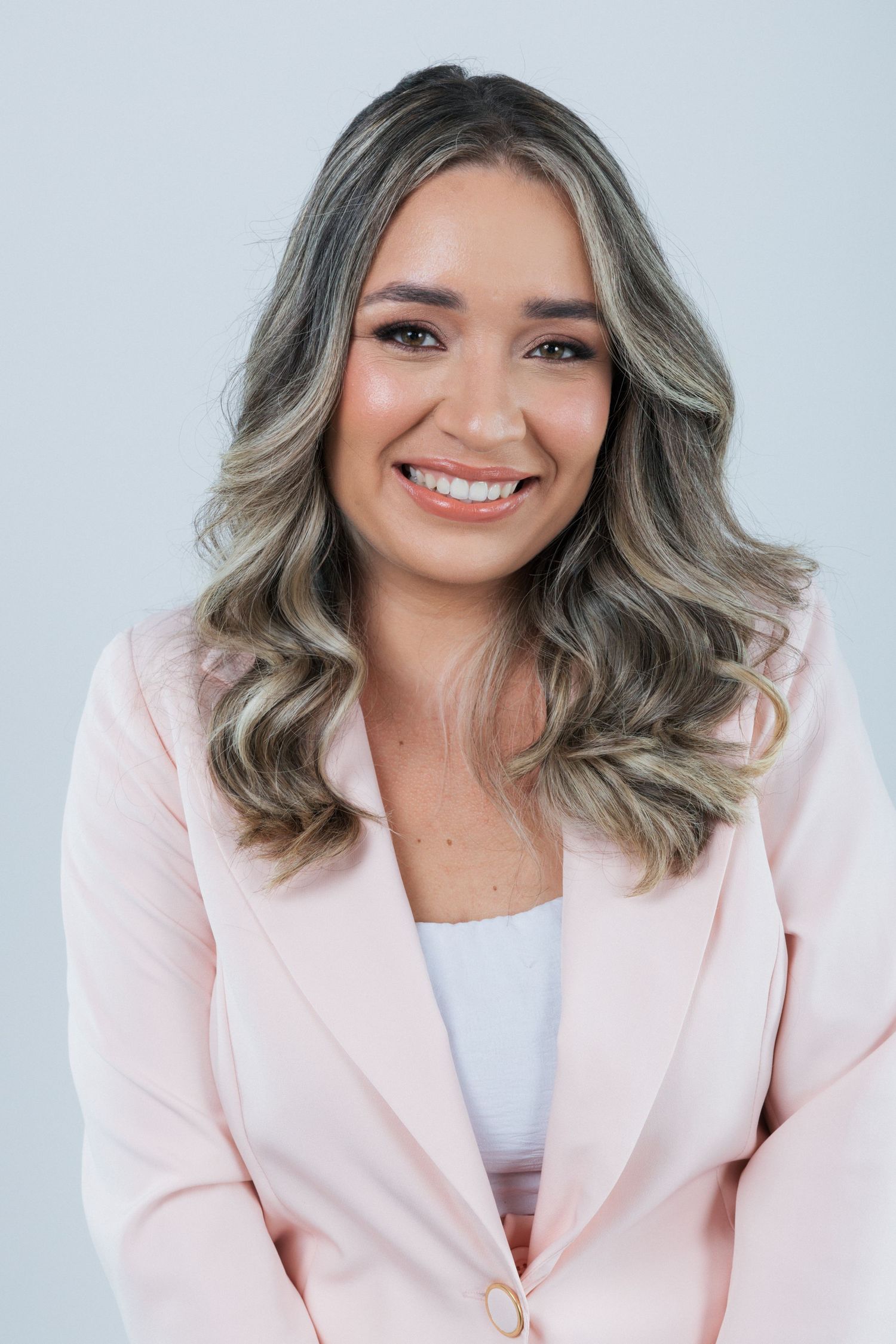Professional portrait of someone wearing a light pink blazer and white top with styled silvery wavy hair.