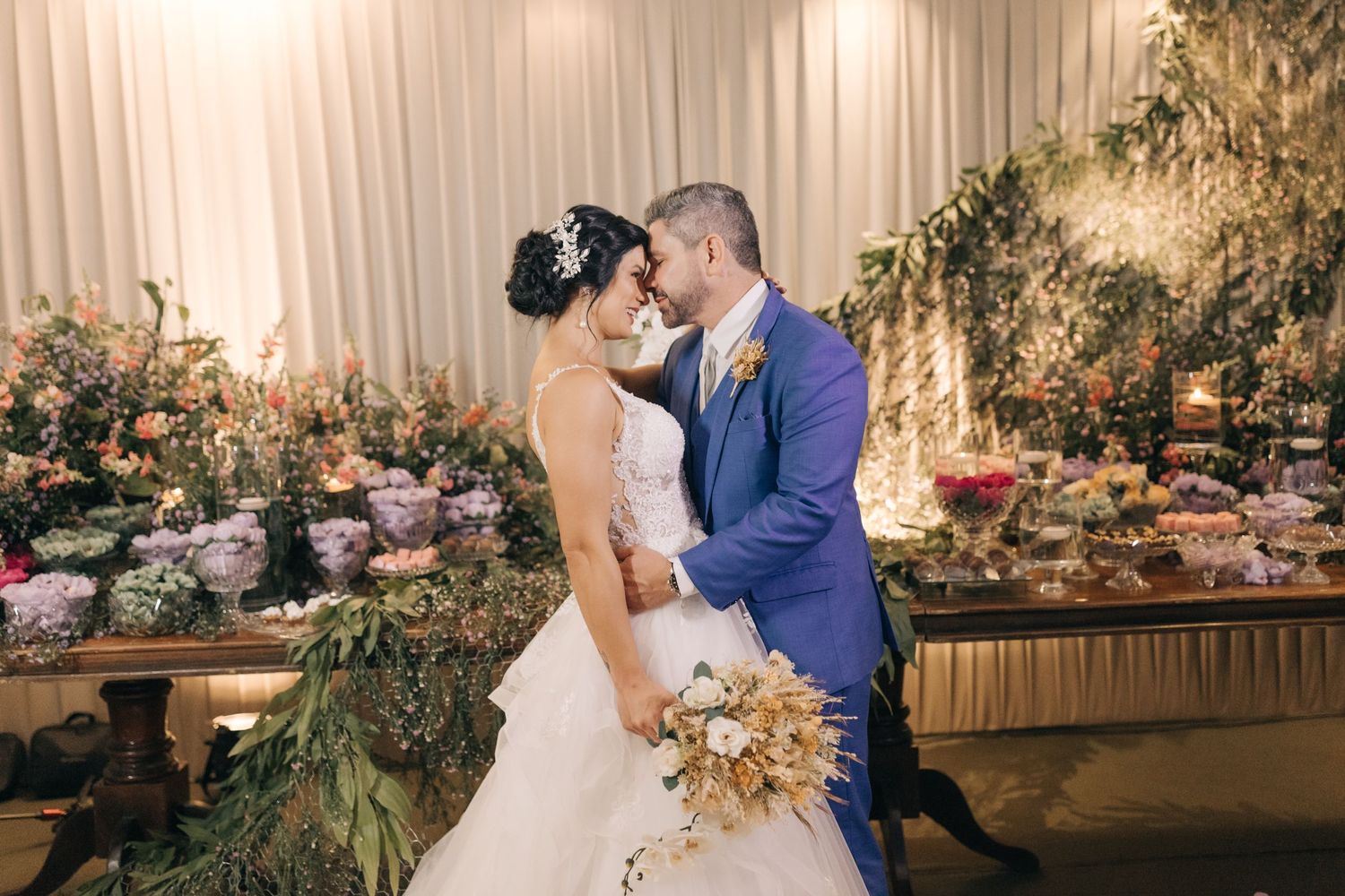 Two newlyweds share an intimate moment in front of a floral wall at their wedding reception.