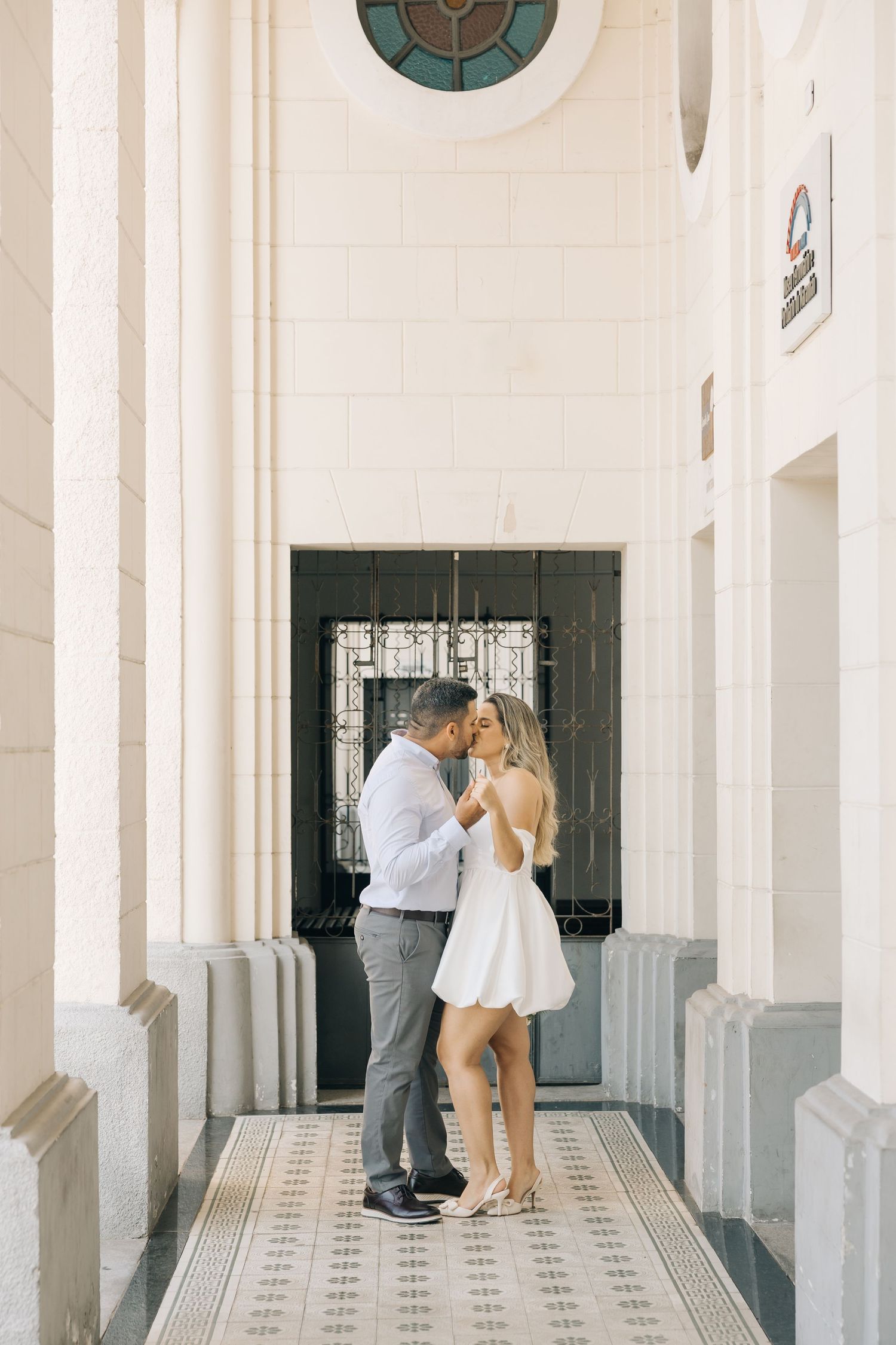 A romantic moment between a couple in a white hallway with ornate tiled floors and architectural columns.