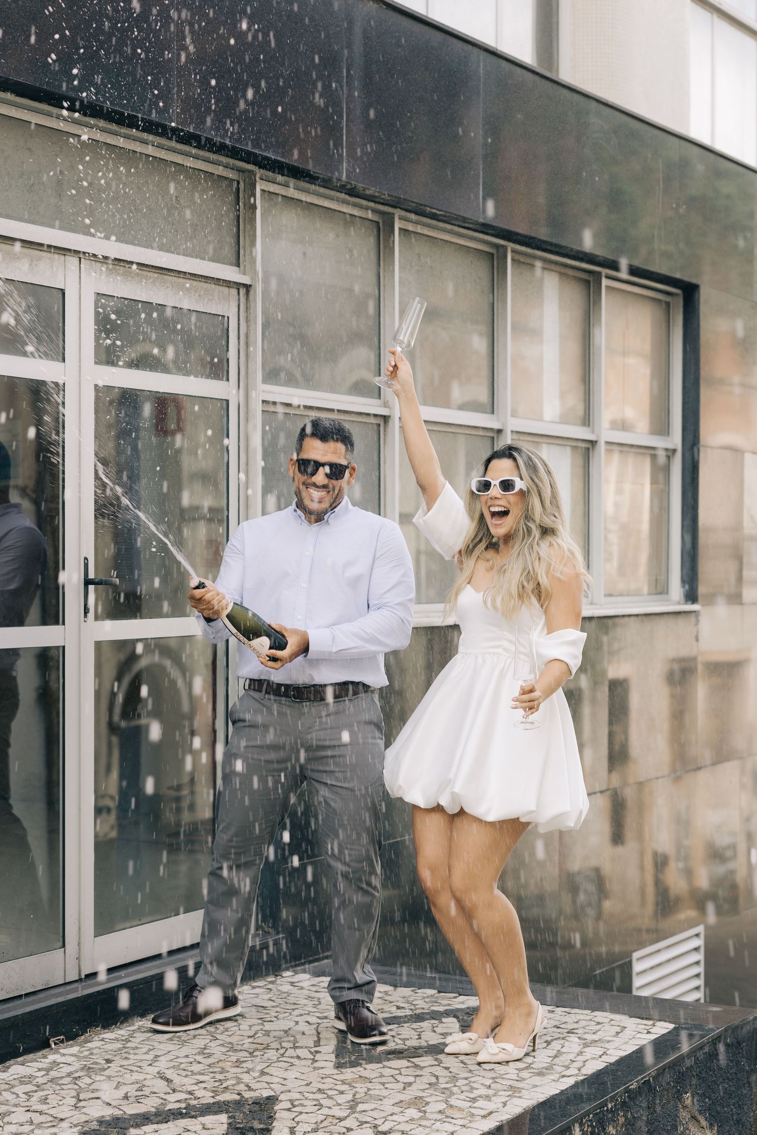A celebratory moment with champagne spray outside a modern building with glass windows.
