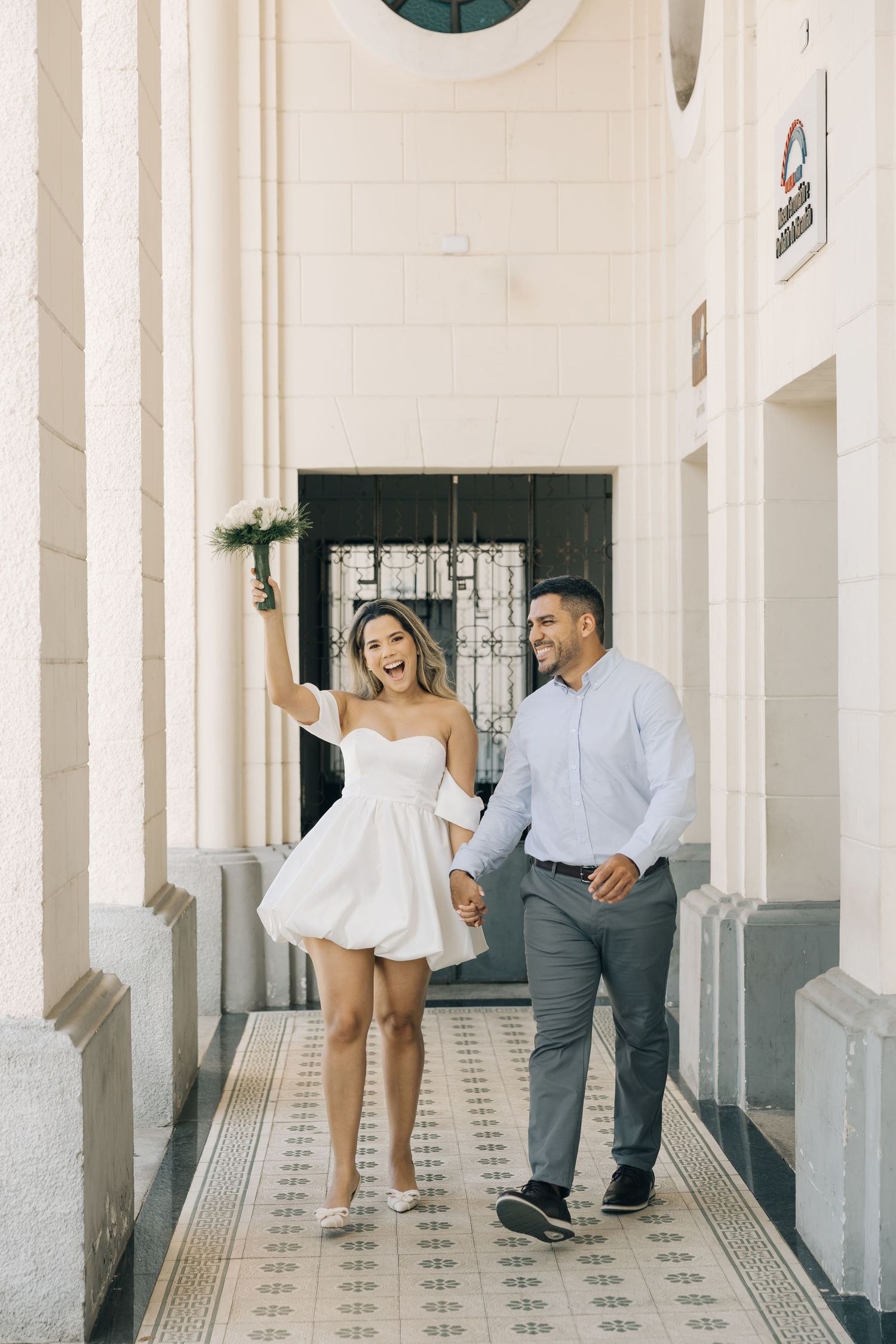 A joyful couple strolling through an elegant hallway with patterned tile flooring.