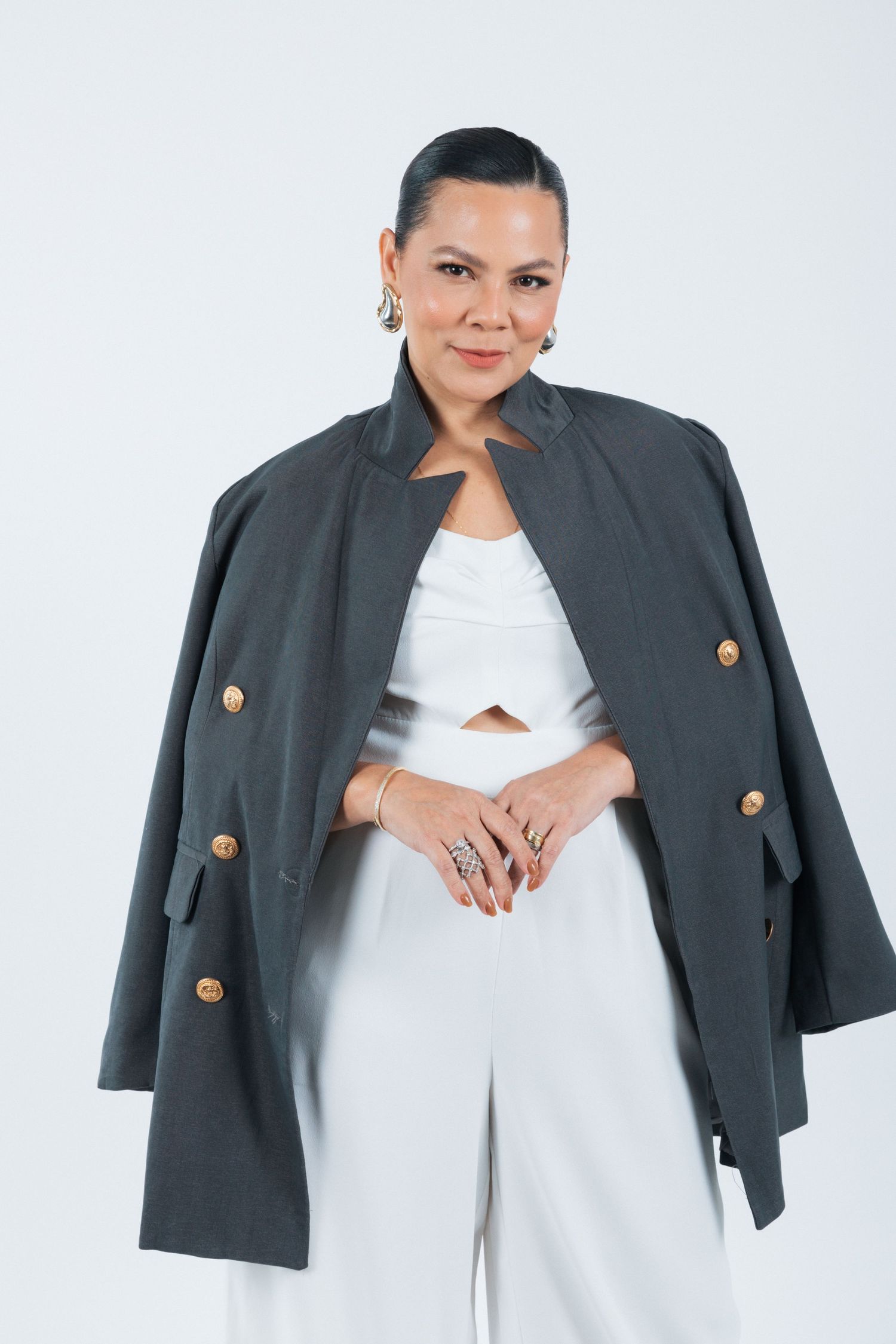 Professional fashion portrait showing a grey blazer worn cape-style over white outfit against white background.