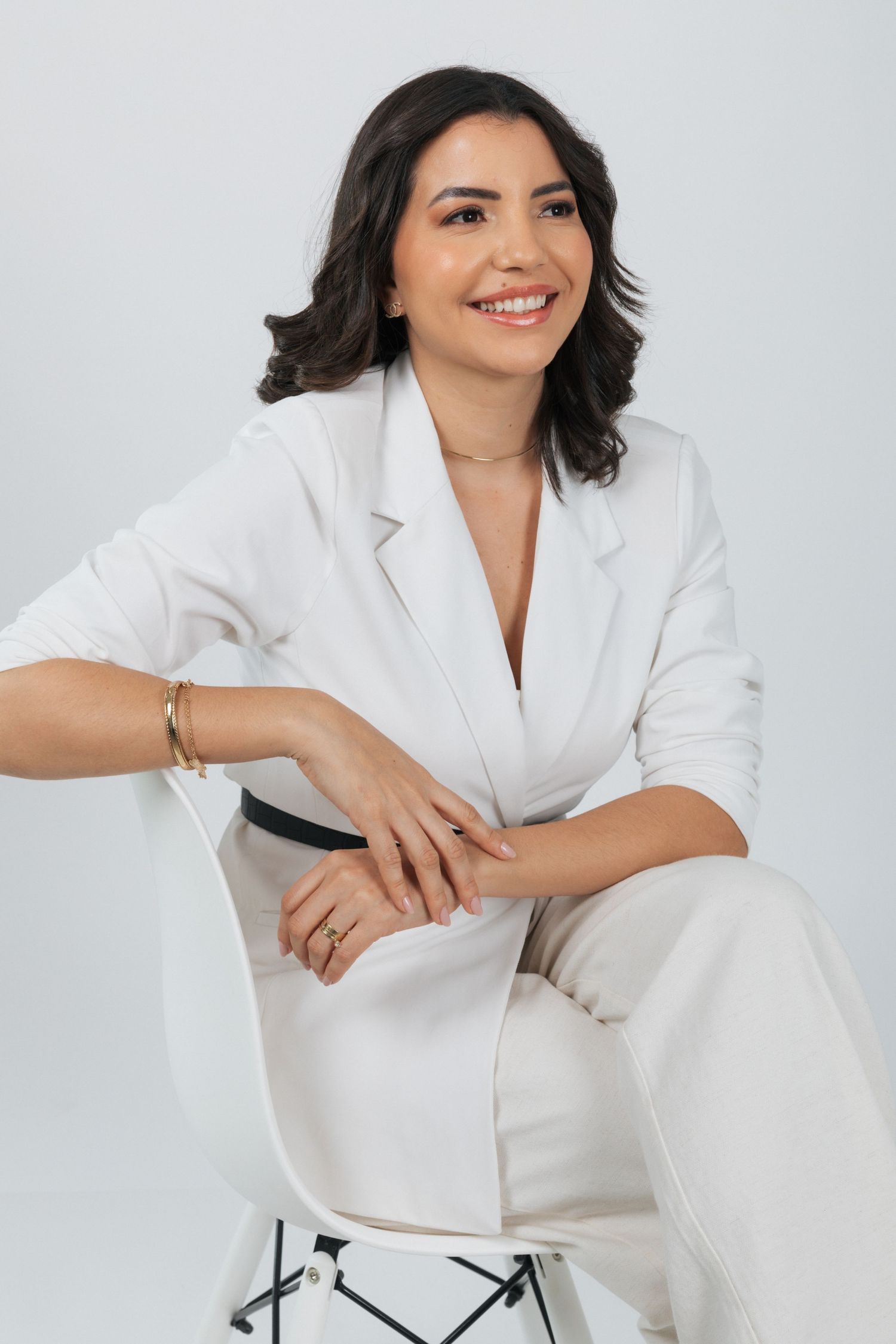 Professional portrait of woman in crisp white blazer seated elegantly on chair.