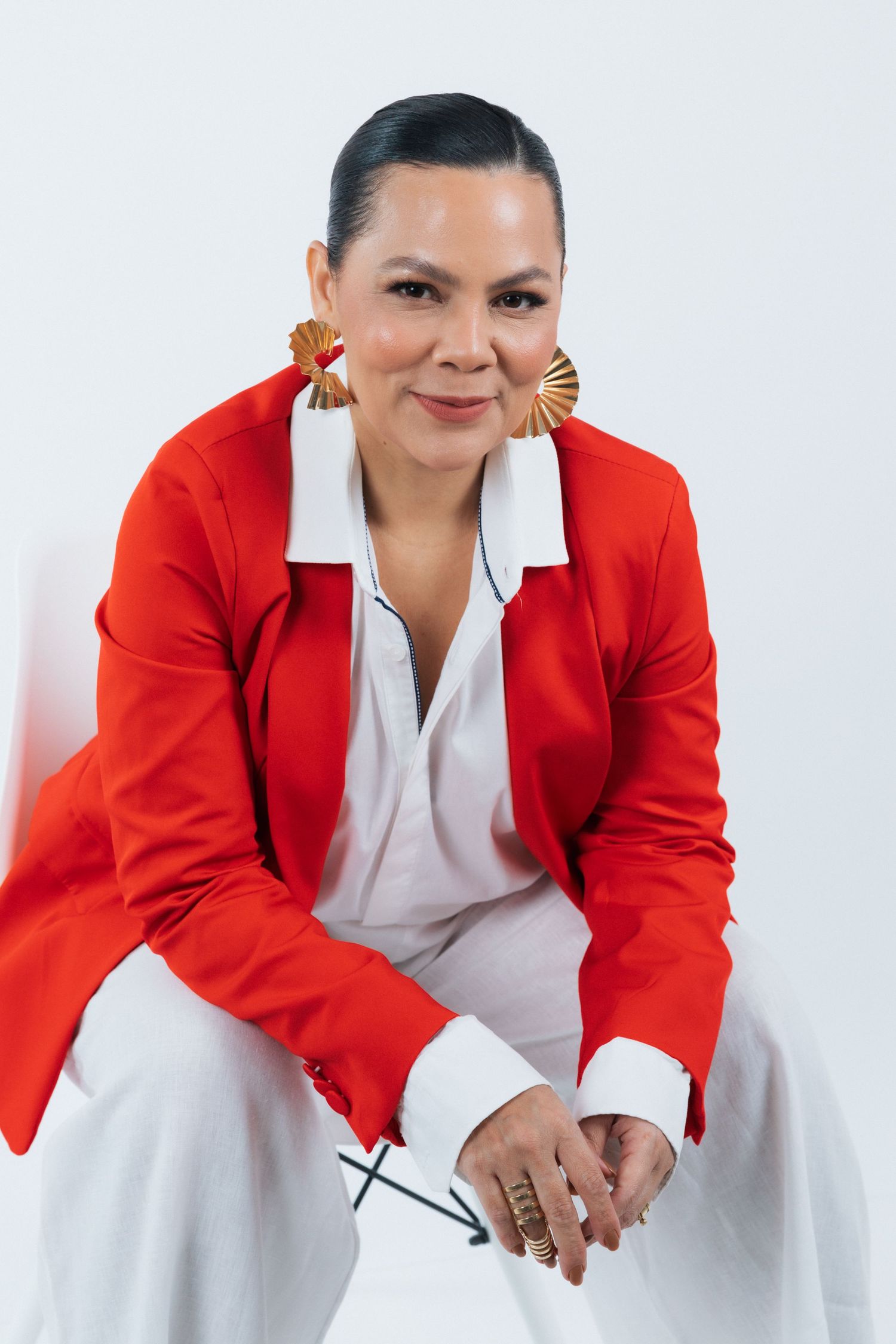 Professional studio portrait showing a bright red blazer, white attire and statement fan earrings.