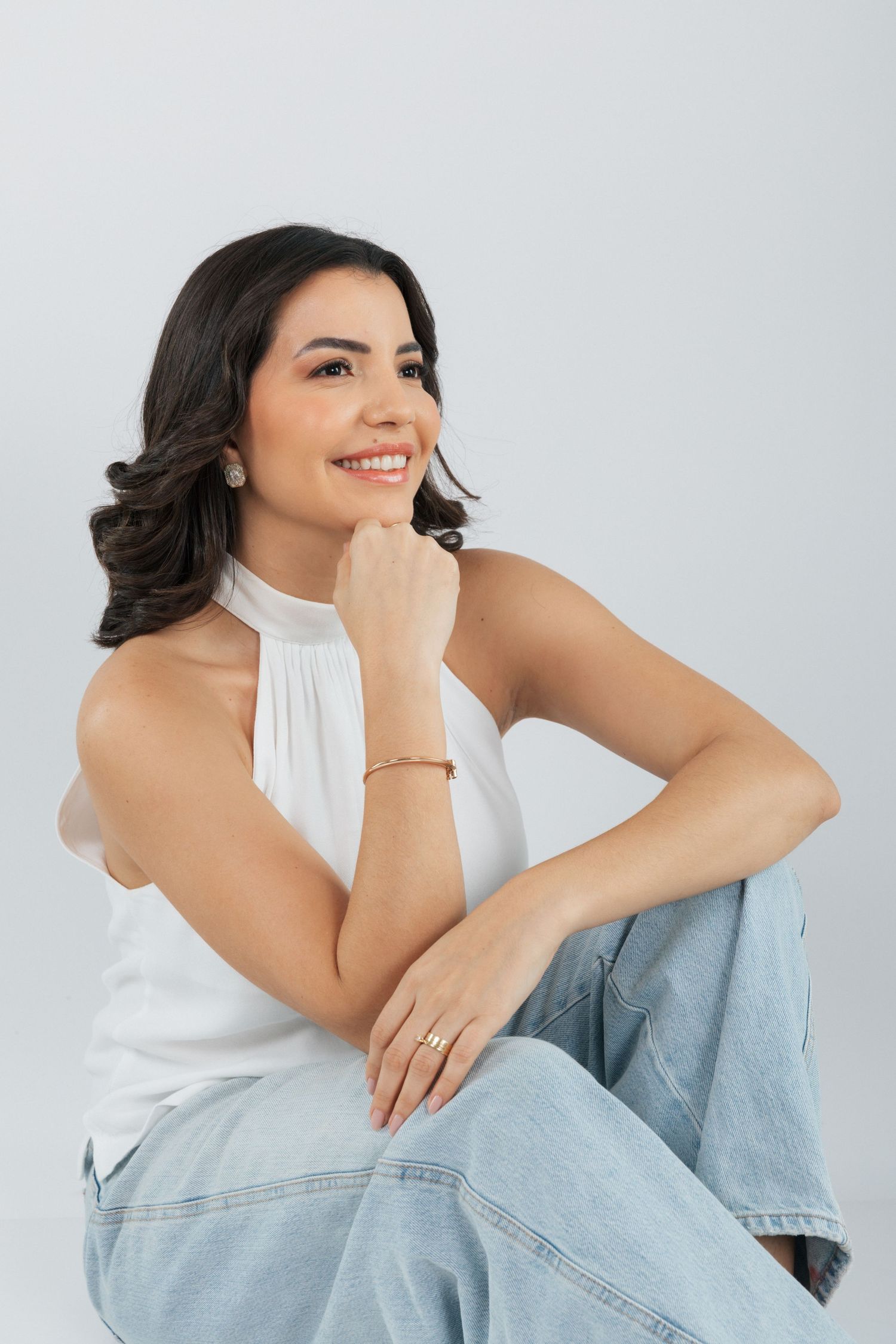 Casual portrait of woman in white top and jeans posing thoughtfully with hand near face.