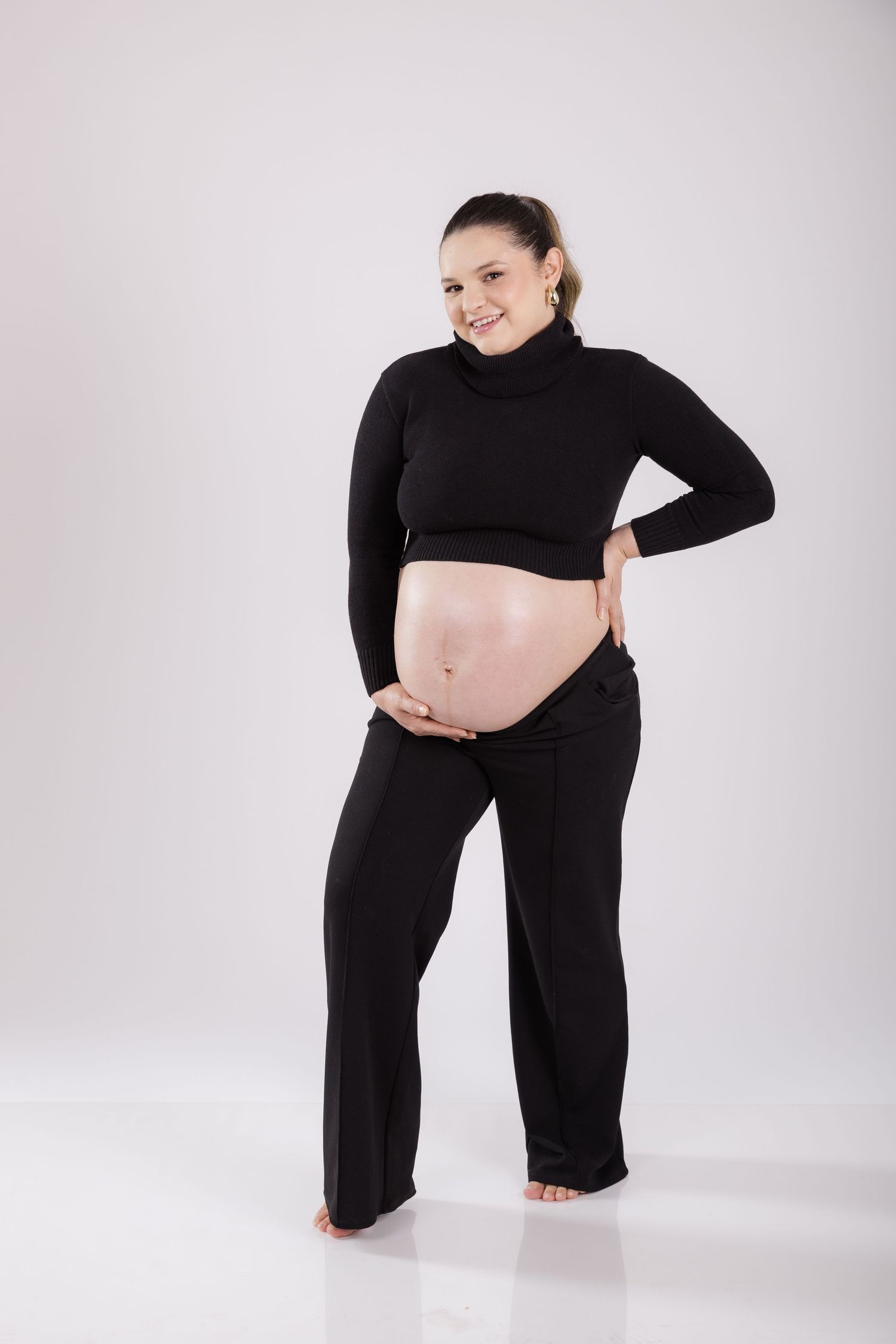 A pregnant woman poses in black activewear against a white background, cradling her bare belly.