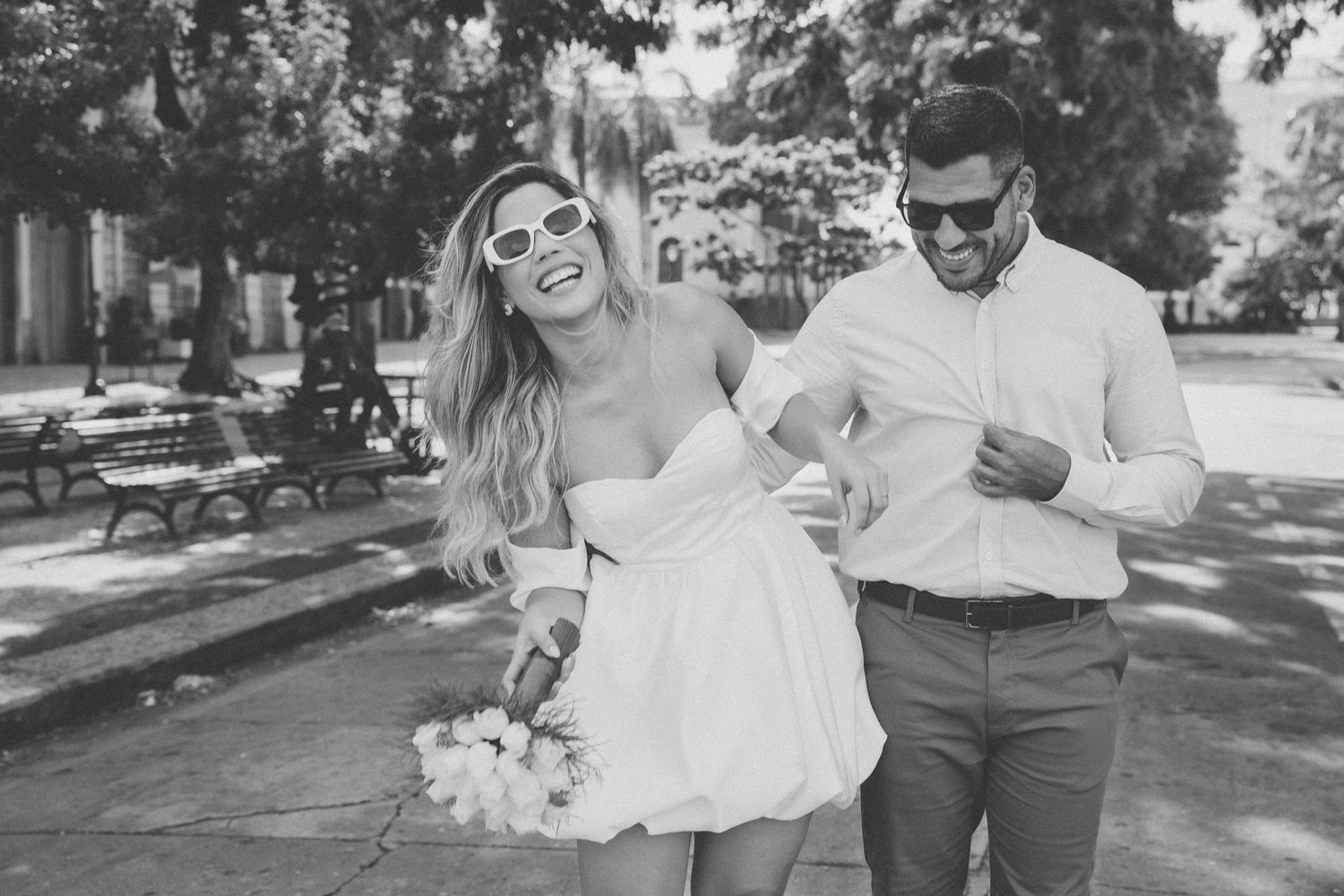 A couple walks together outdoors holding flowers on a sunny summer day in black and white.
