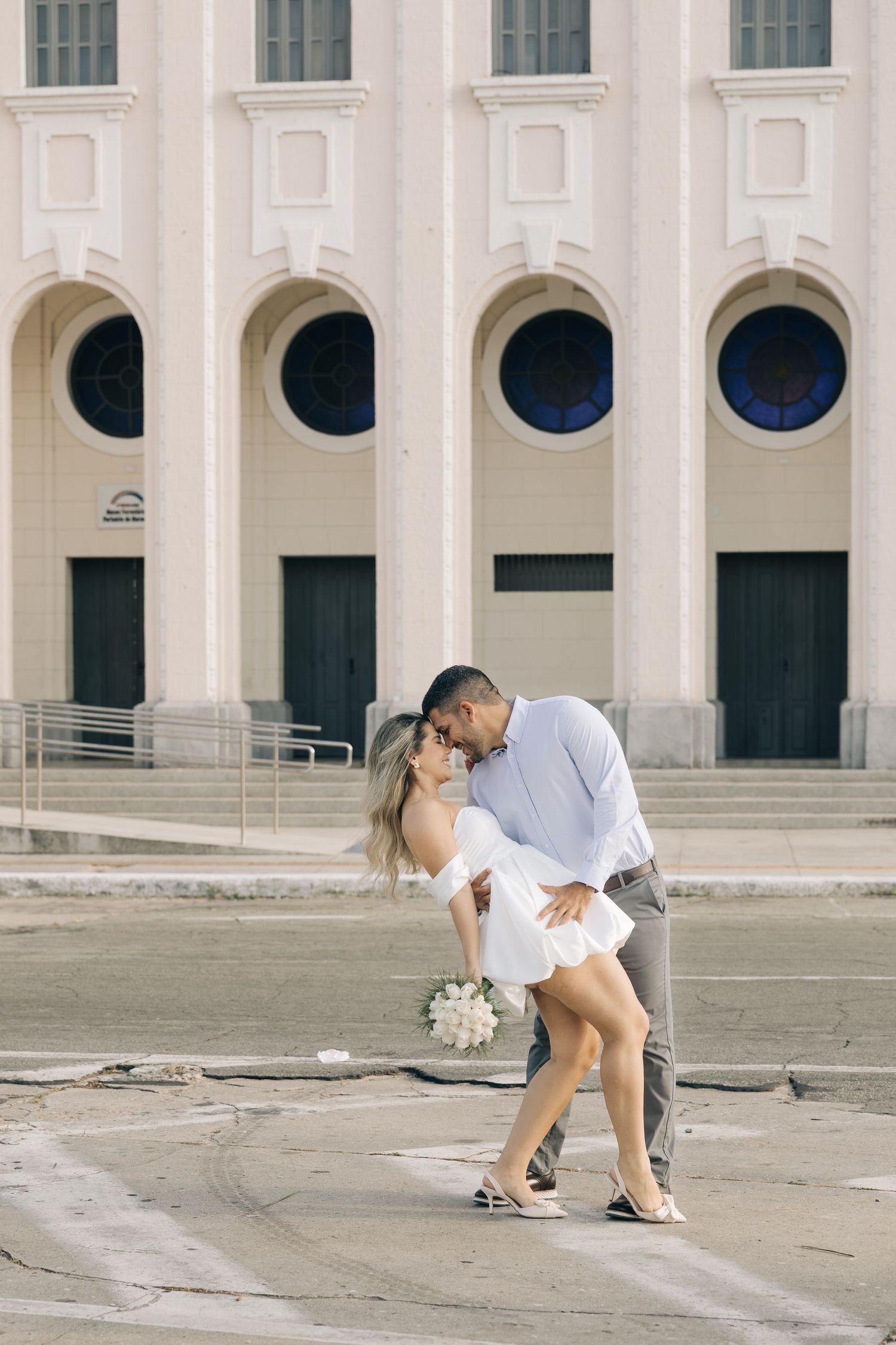 Romantic couple dancing and embracing outside a grand building with arched windows and classic architecture.