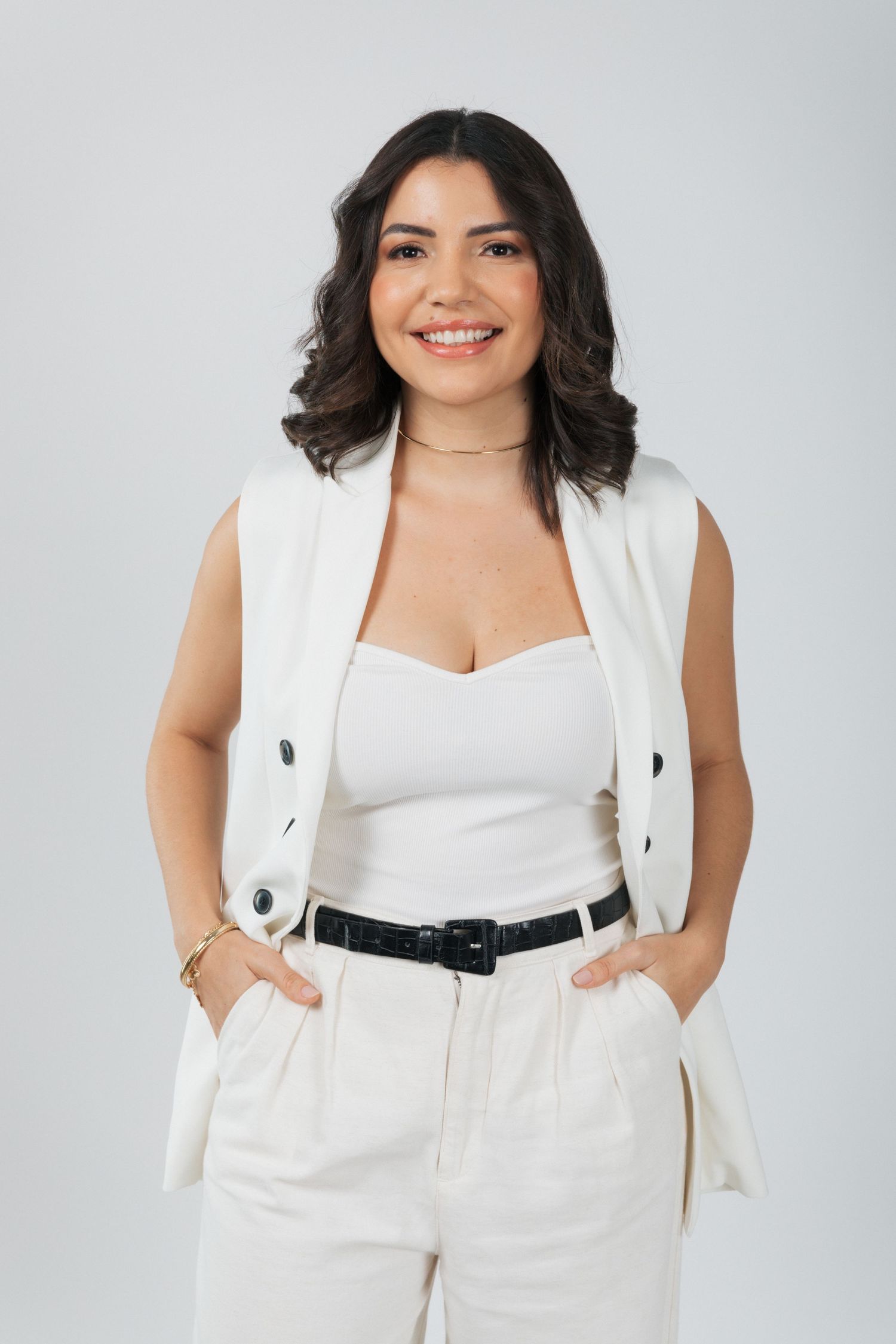 Elegant portrait in white vest and pants with black belt against neutral background.