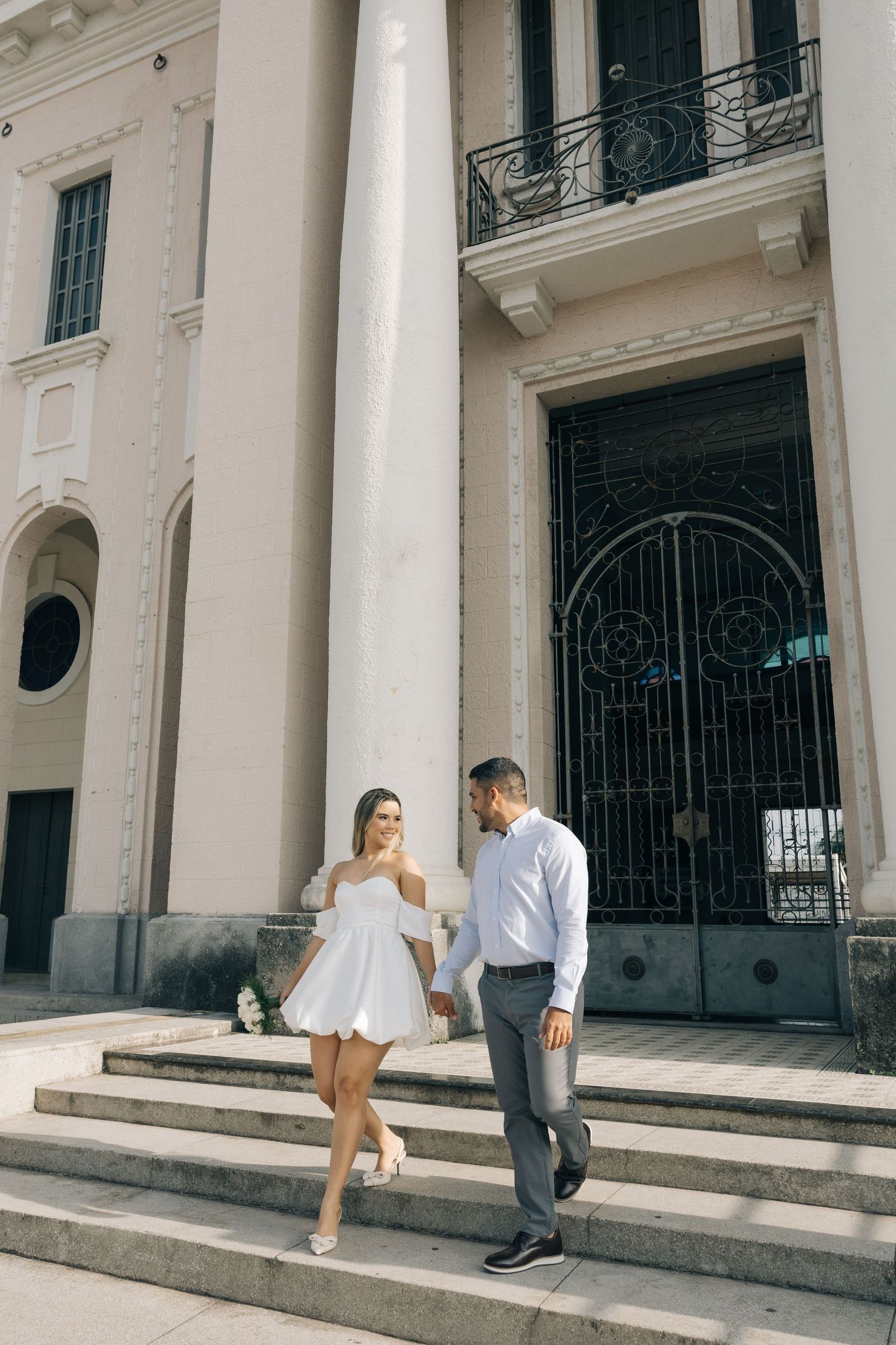 A couple descends elegant stone steps outside a grand building with ornate architectural details and columns.