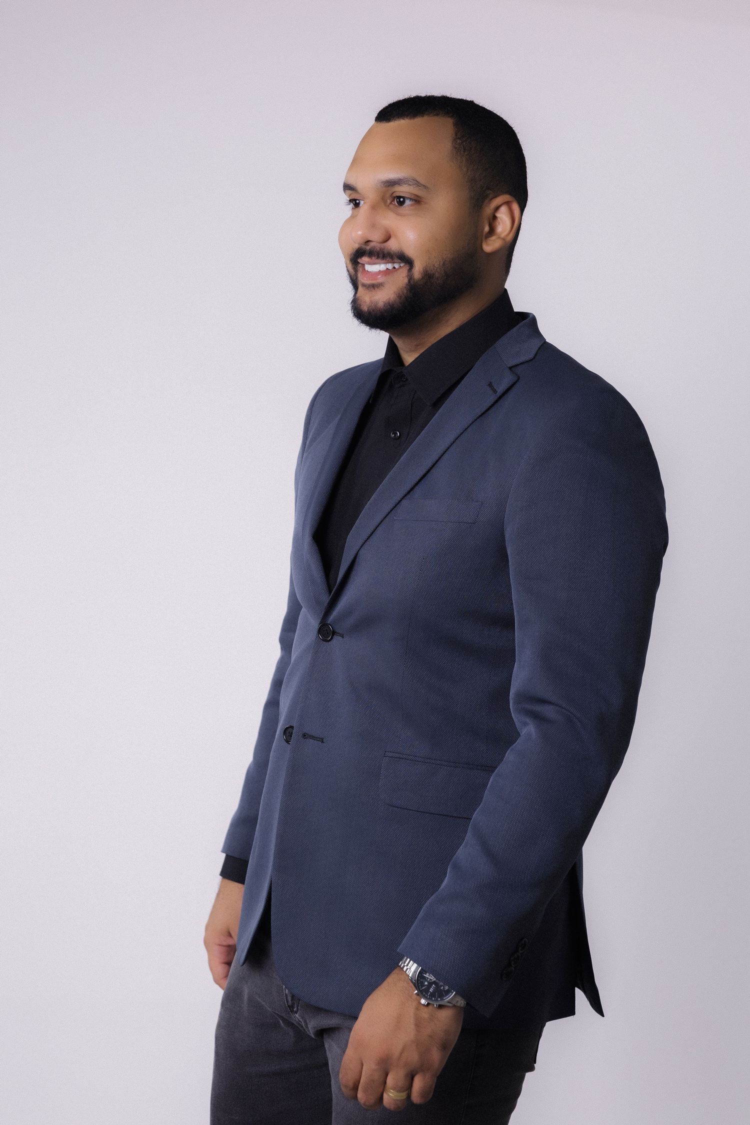 Professional portrait of someone in a navy blazer and black shirt against a light backdrop, smiling warmly.