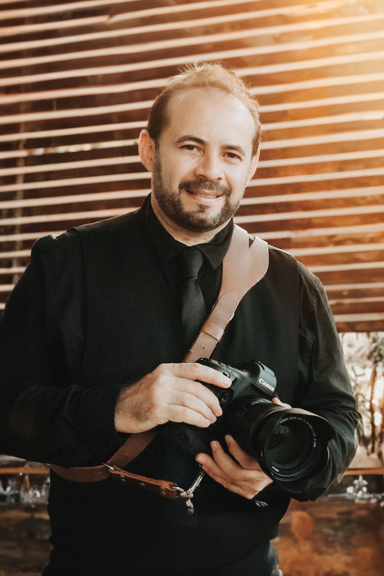 A series of warm-toned images showing someone in black clothing holding and examining a camera with wooden slats in background.