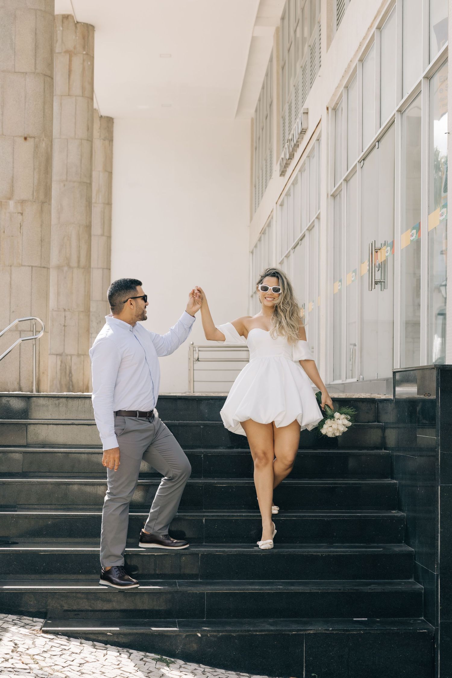 A couple celebrates on stone steps outside a modern building with white columns.