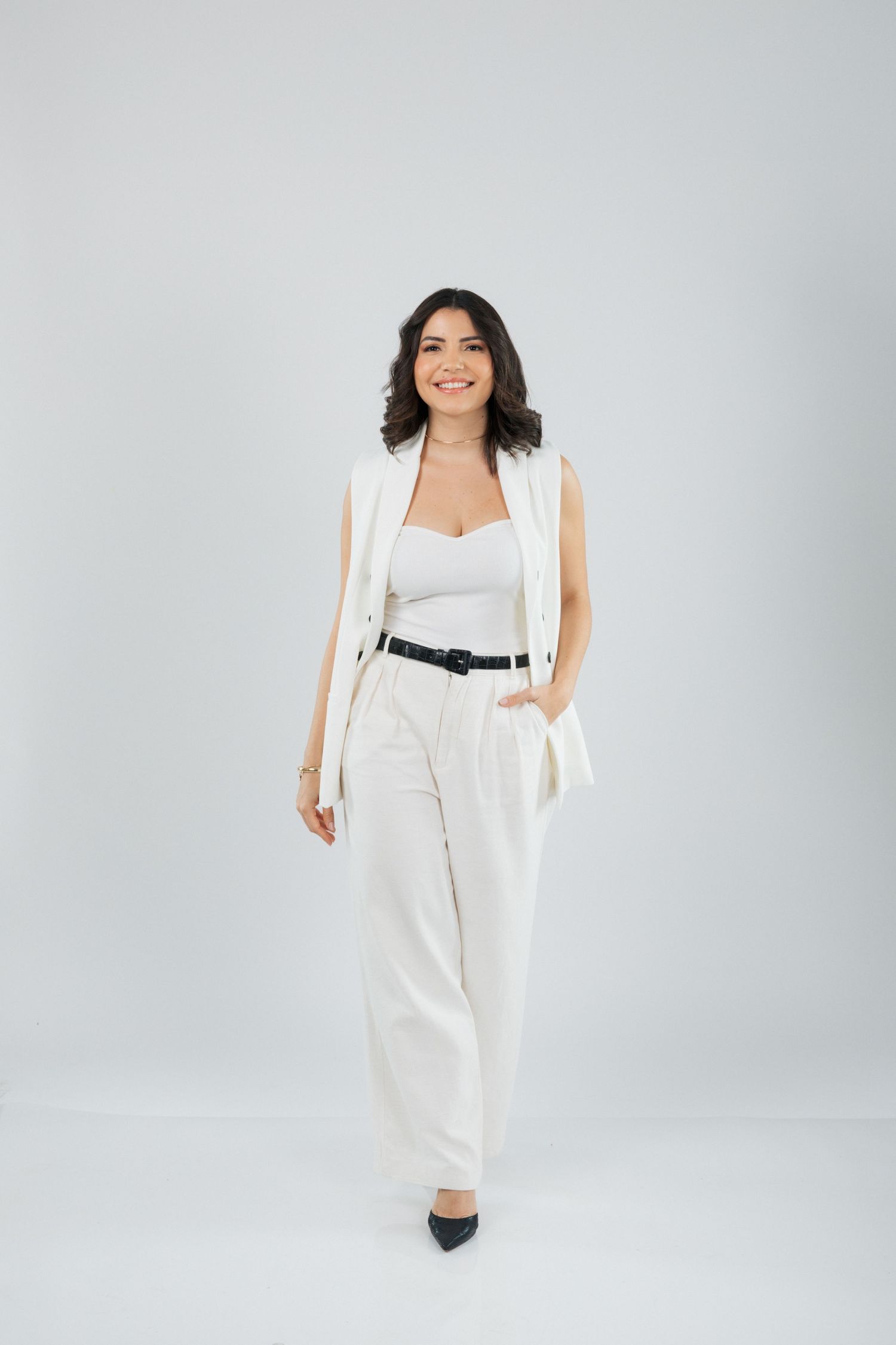 Full-length fashion shot of white pantsuit with black belt and heels.