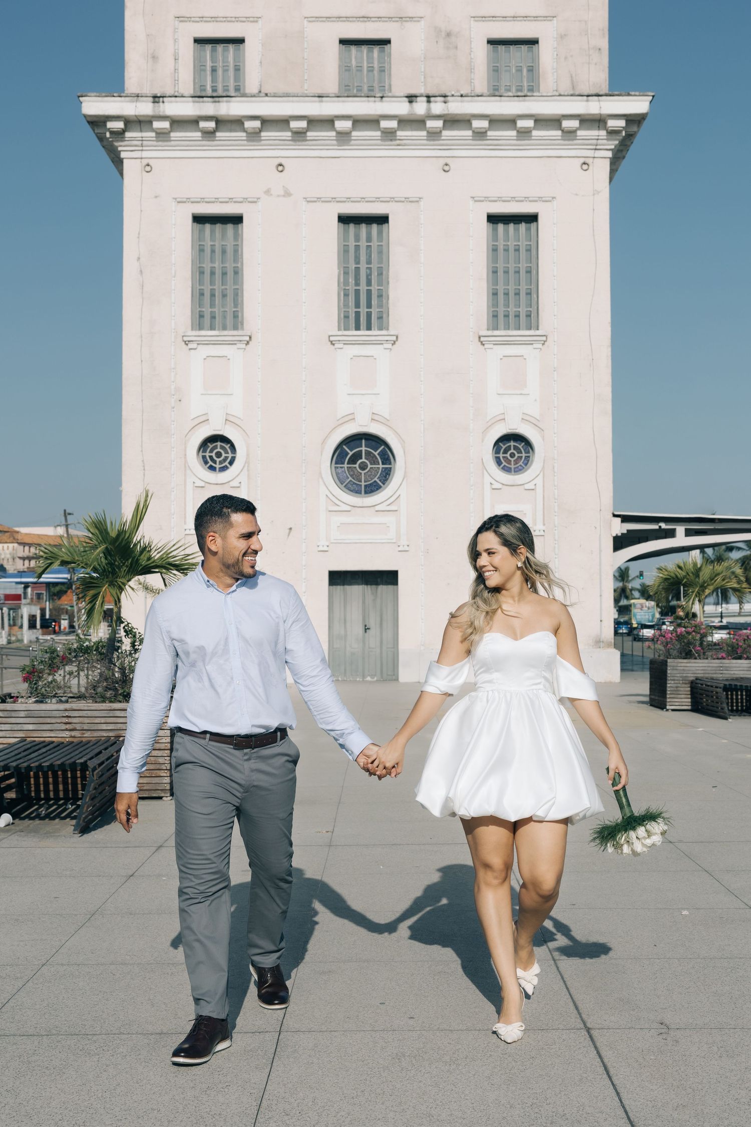 A couple strolling together against the backdrop of a classic white building with circular windows.