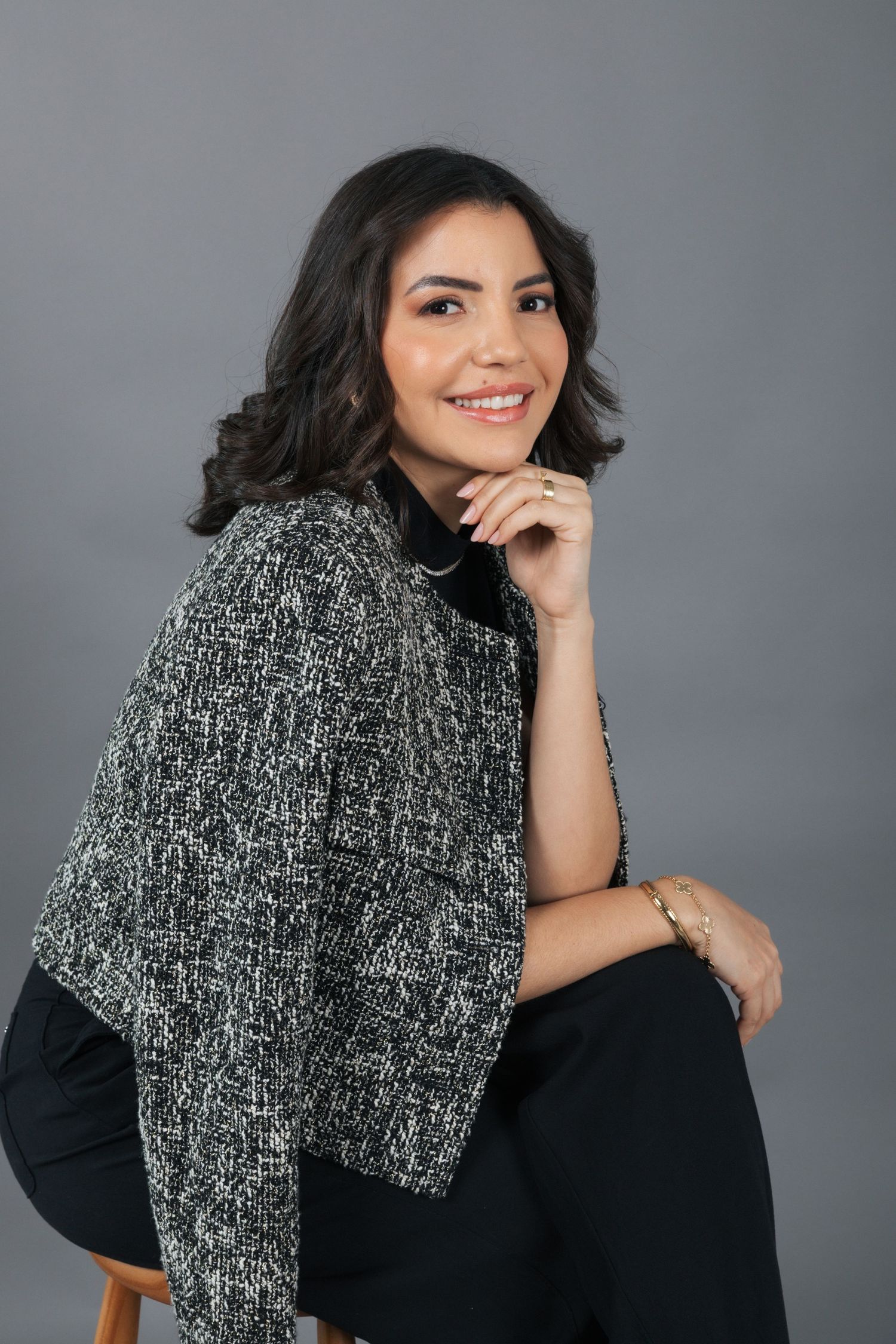 Stylish person in textured tweed jacket and black turtleneck poses elegantly against grey background.
