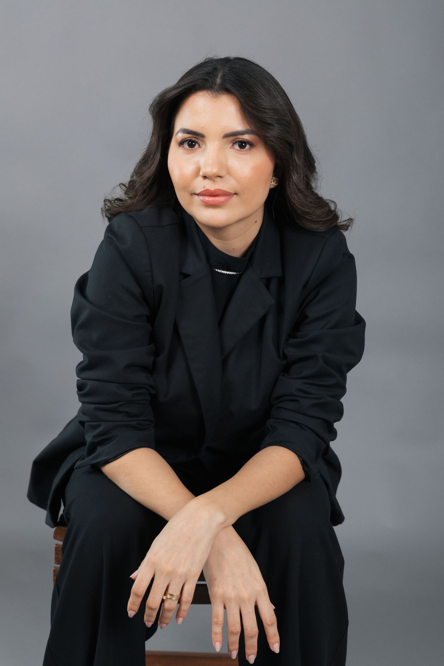Professional studio portrait showing relaxed pose in all-black attire against gray background.