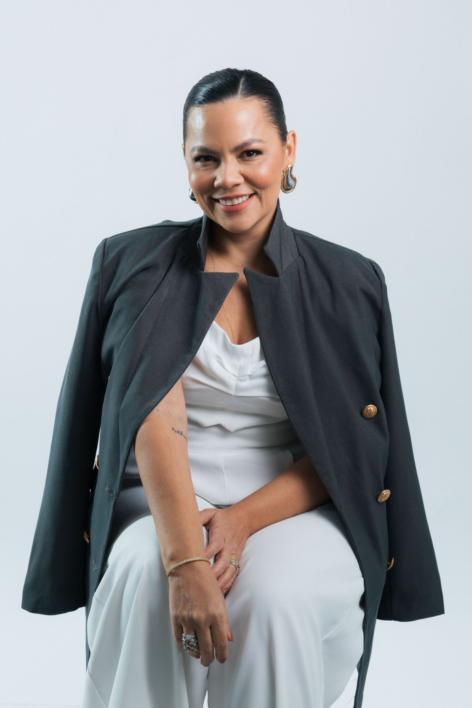 Professional portrait of a person wearing a black blazer over a white dress against a light background.