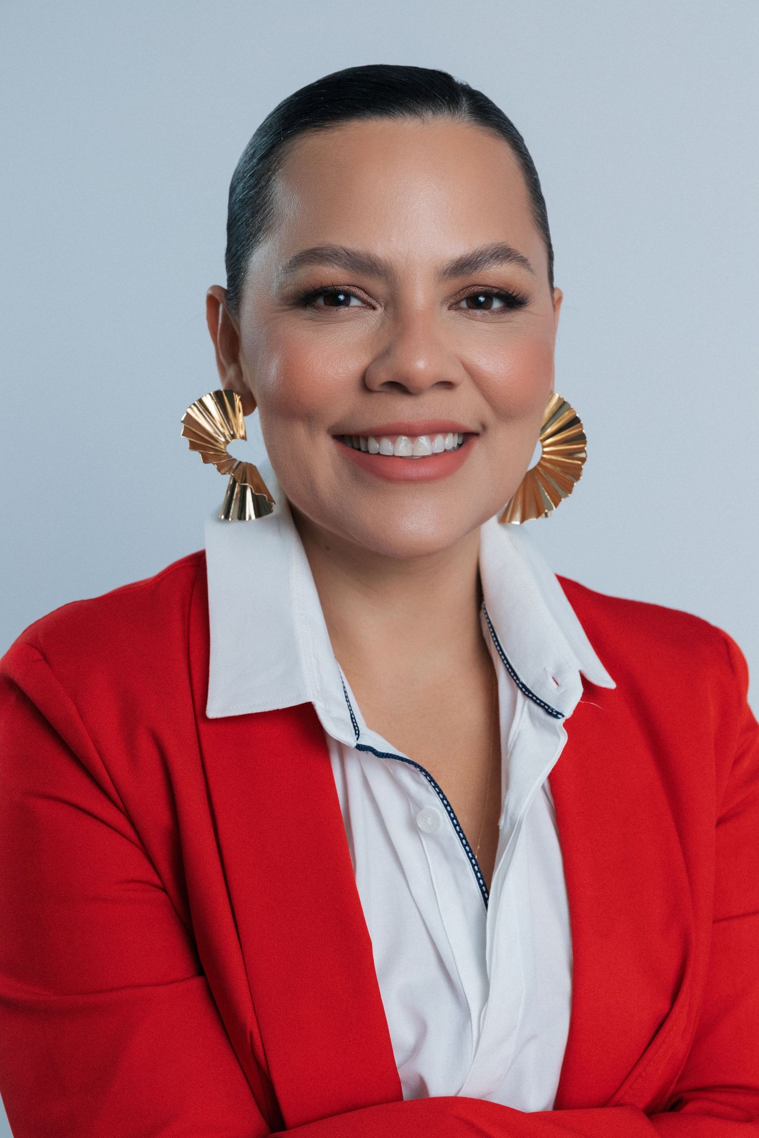Stylish portrait featuring statement gold fan earrings and a vibrant red blazer with white collar detail.