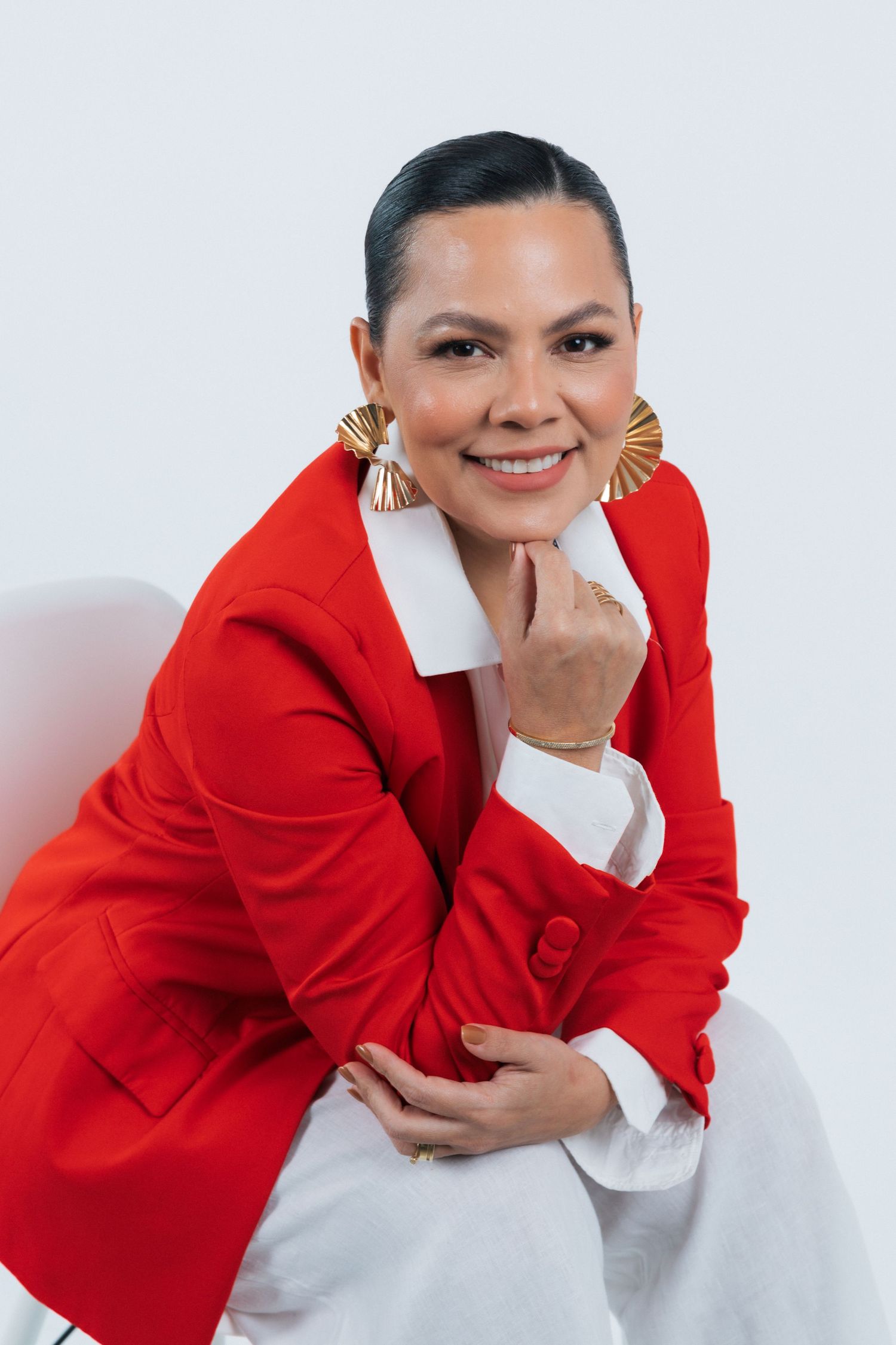 Fashionable portrait of model in red blazer with statement earrings against white backdrop.