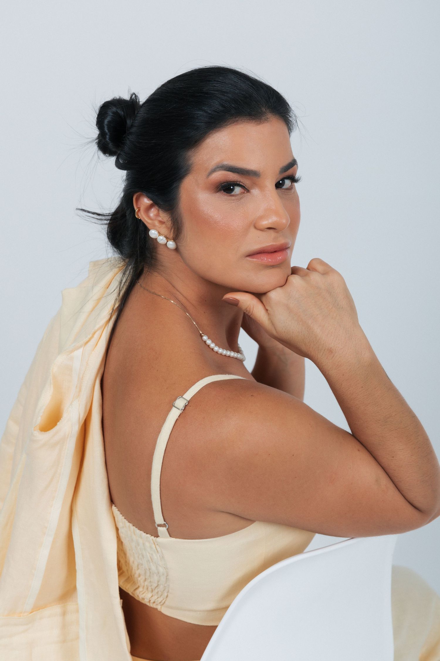 Fashion portrait of a model wearing cream outfit and pearl necklace in elegant pose against studio backdrop.