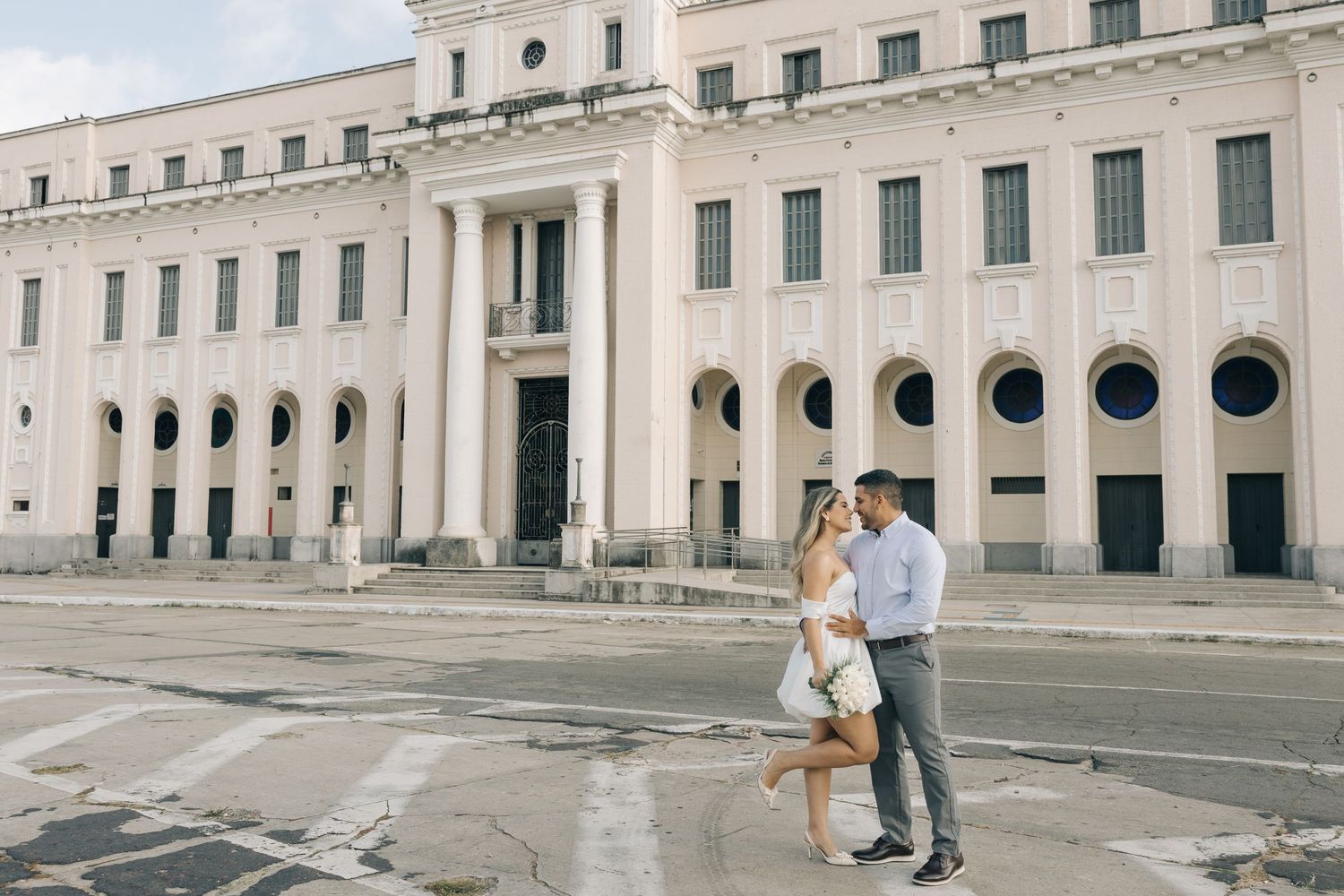 Couple embraces in front of a grand white neoclassical building with circular windows and columns.