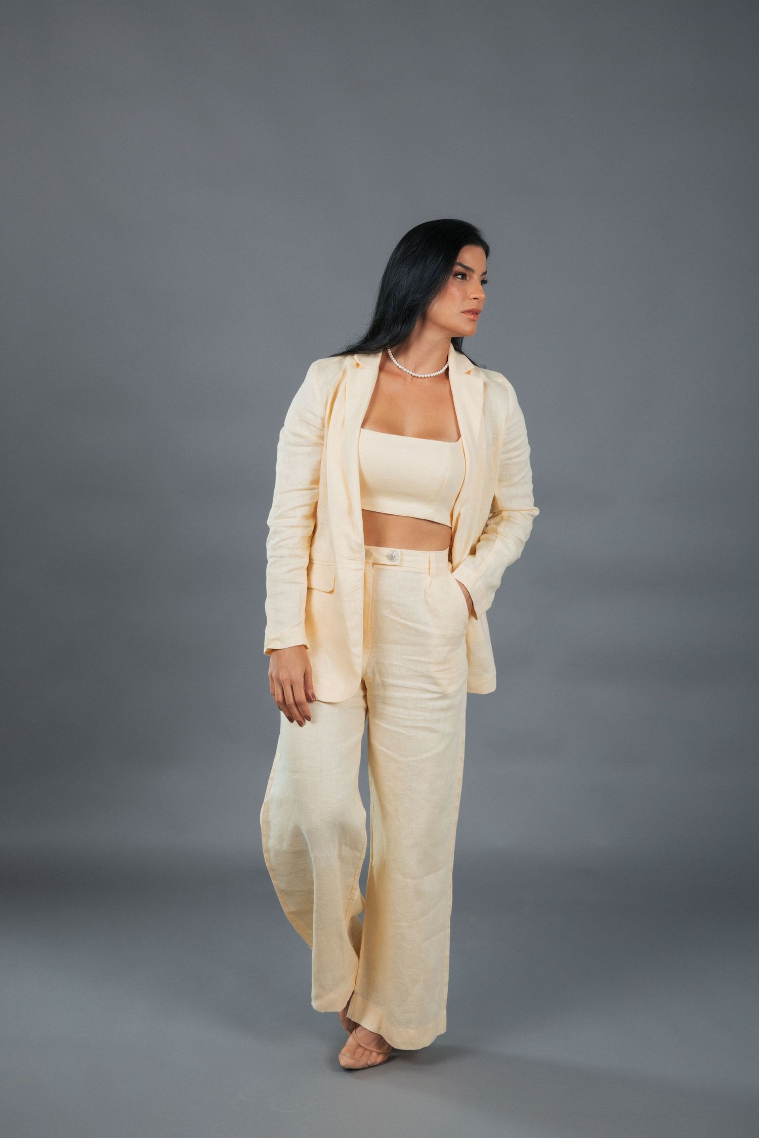Stylish cream-colored pantsuit outfit with crop top and wide-leg trousers on grey studio background.