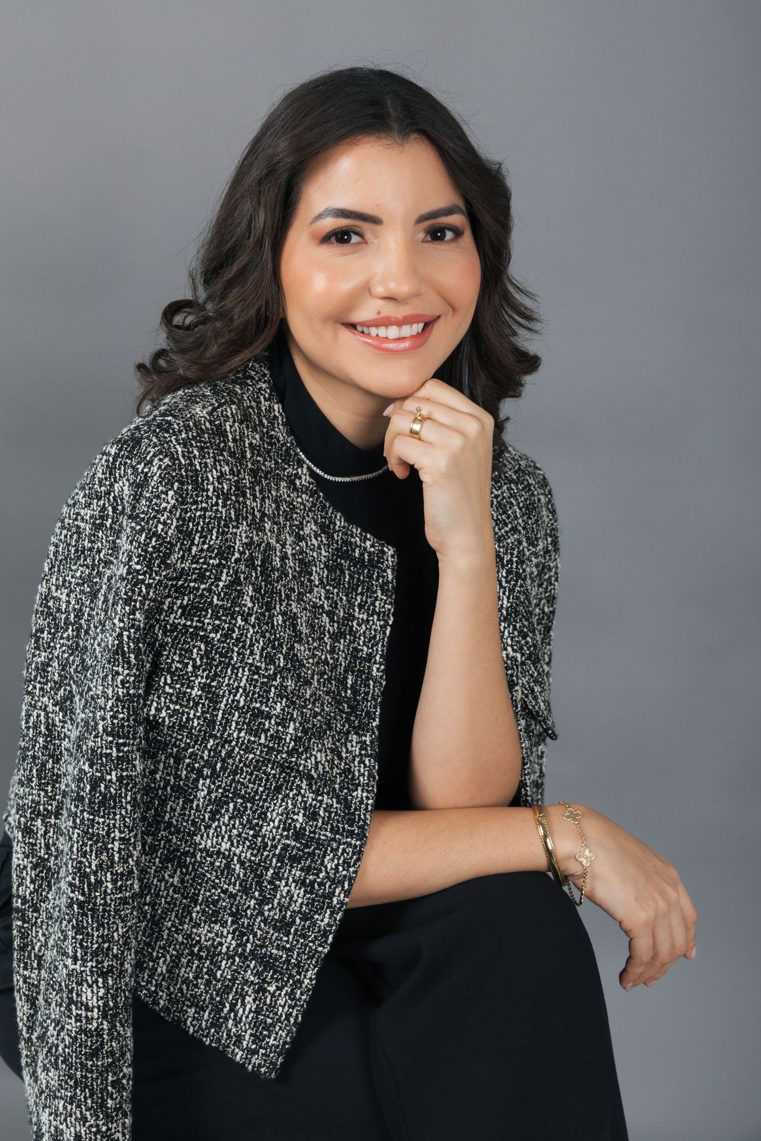 Business portrait featuring a woman in a textured tweed jacket and black turtleneck against a gray backdrop.