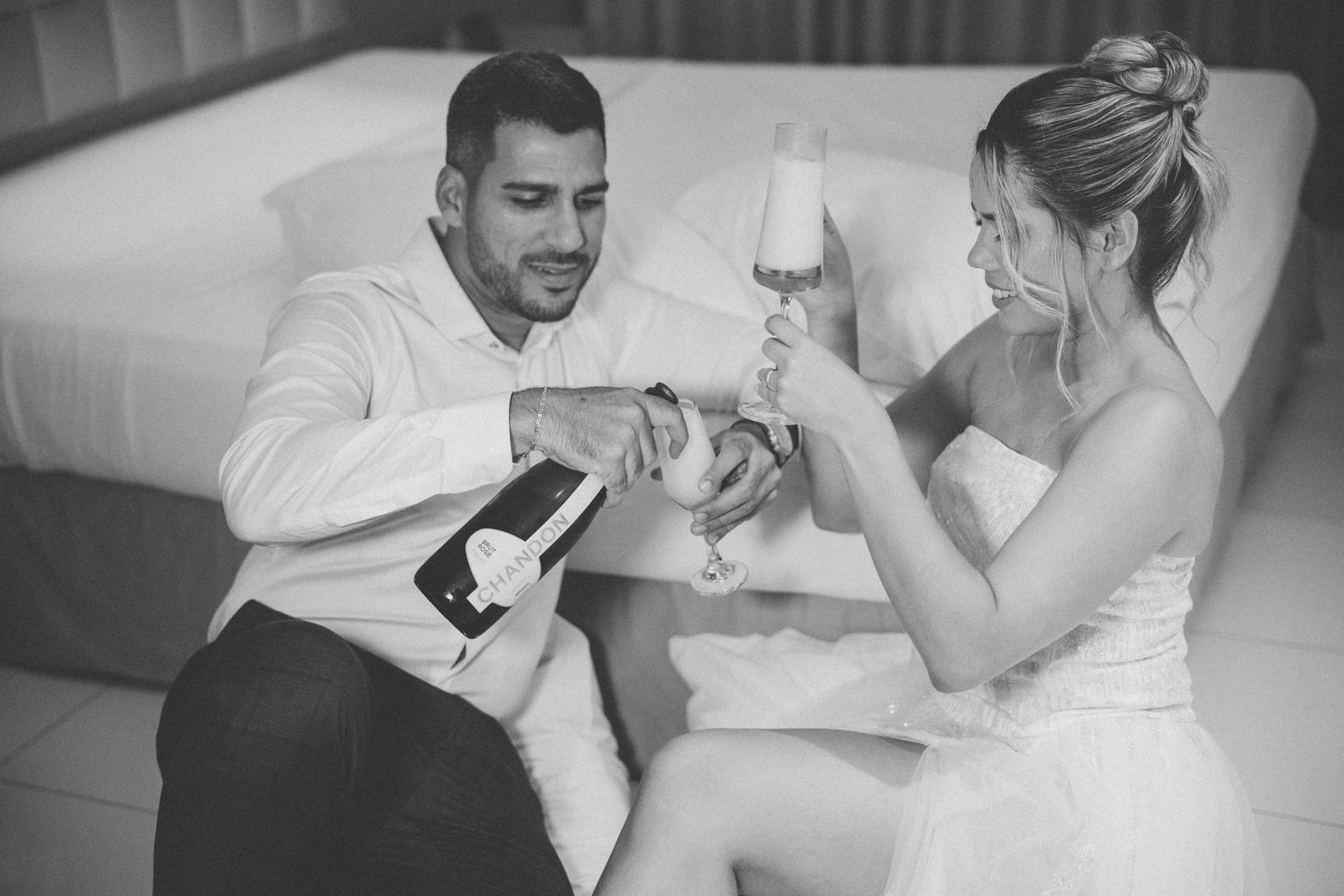 A couple celebrates with champagne while sitting together on a white couch.